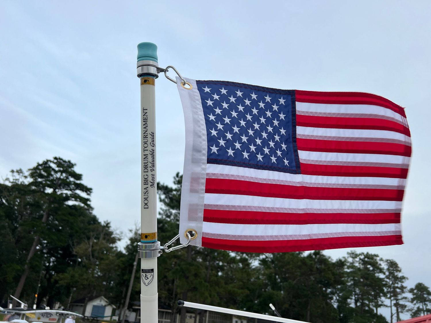 DOUSA MVG Flag holder with American flag waving in breeze against blue sky with trees in background.