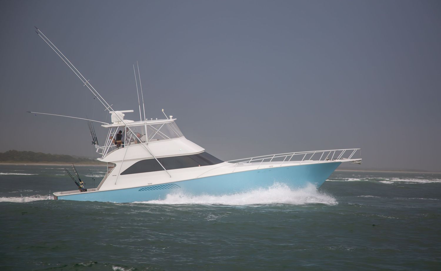 Blue and white sport fishing yacht powers through choppy coastal waters.