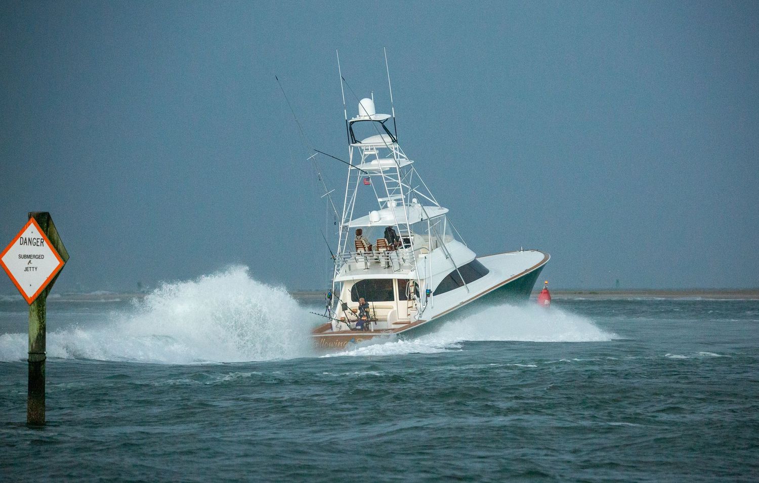 White fishing yacht powers through choppy waters creating large wake in stormy conditions.