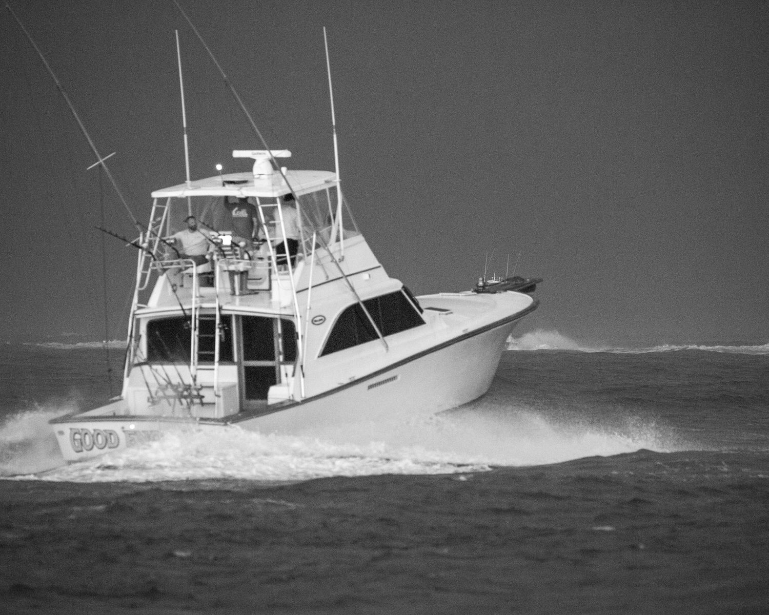 Sport fishing boat powers through heavy waves in black and white.