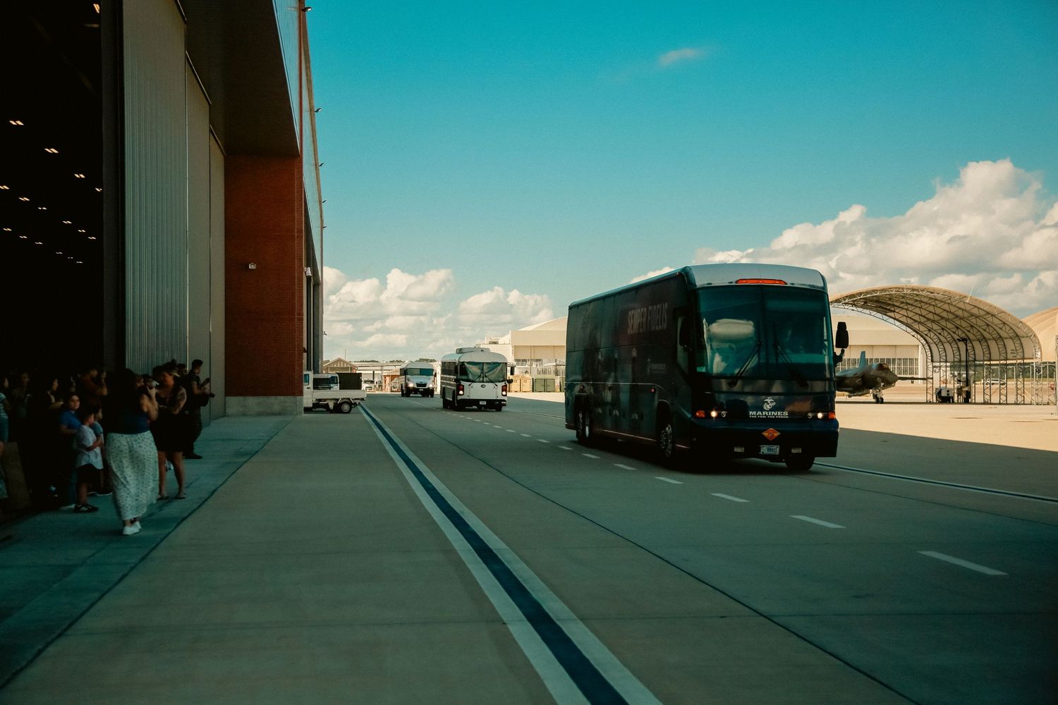 Military aircraft and vehicles line up on an airfield tarmac under bright blue skies.
