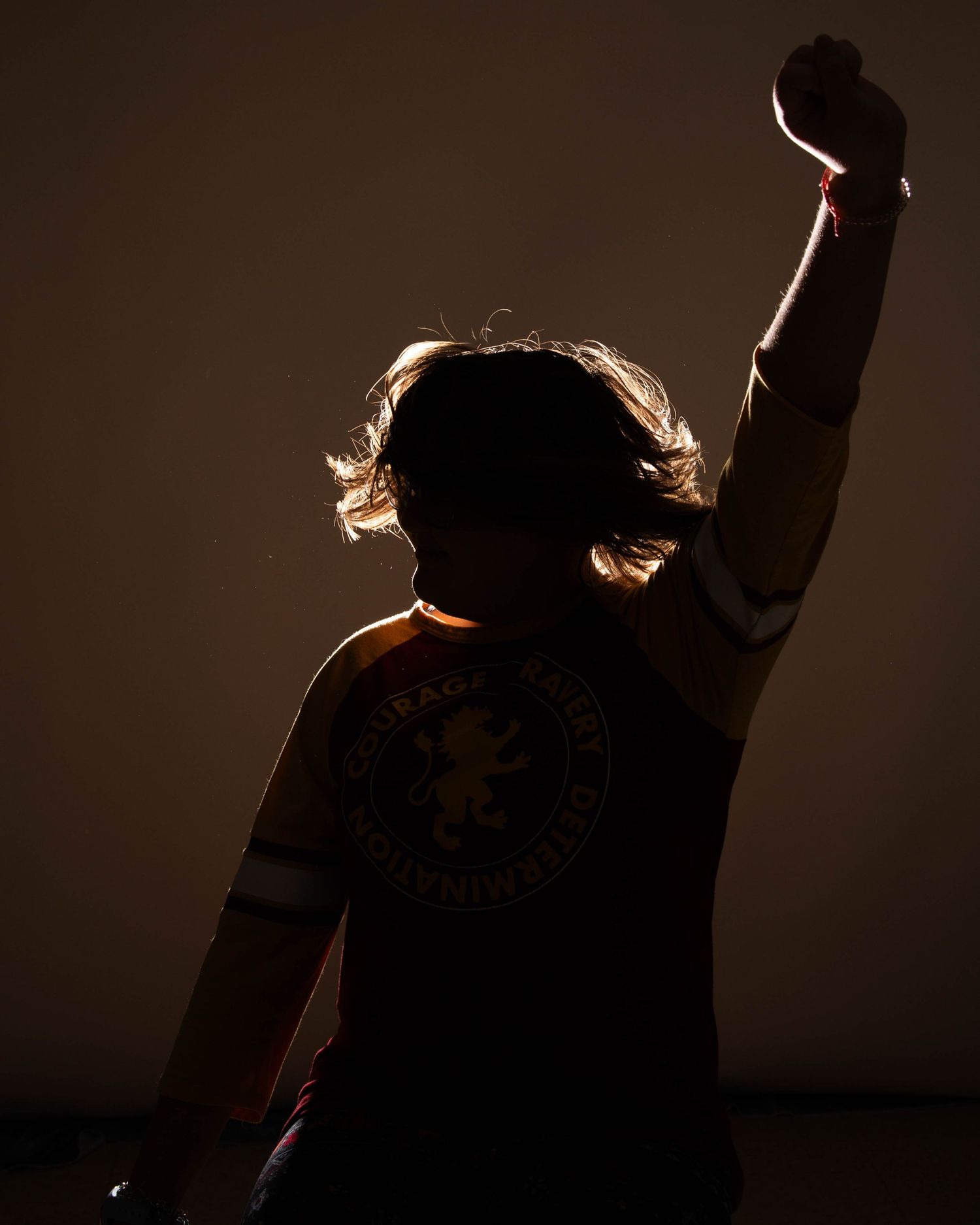 Silhouetted person raising fist wearing Chelsea FC shirt, dramatically backlit against dark background.