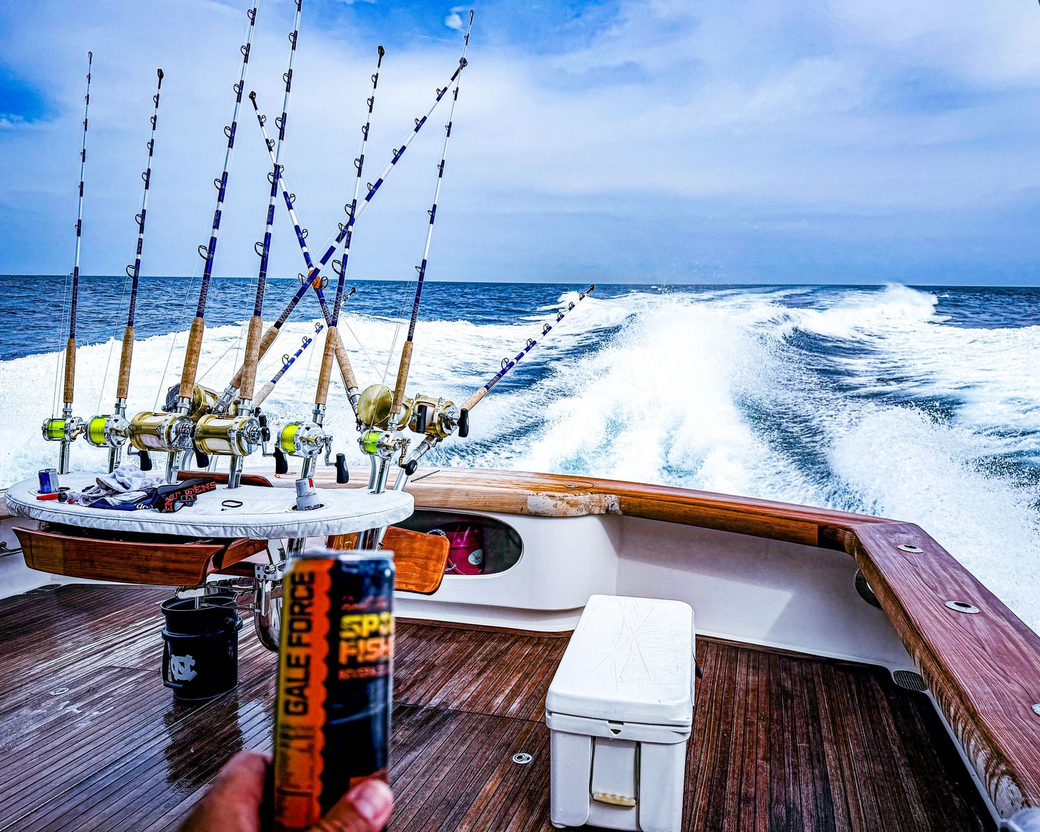 Multiple fishing rods on a speeding sport fishing boat leaving a wake on the open ocean.