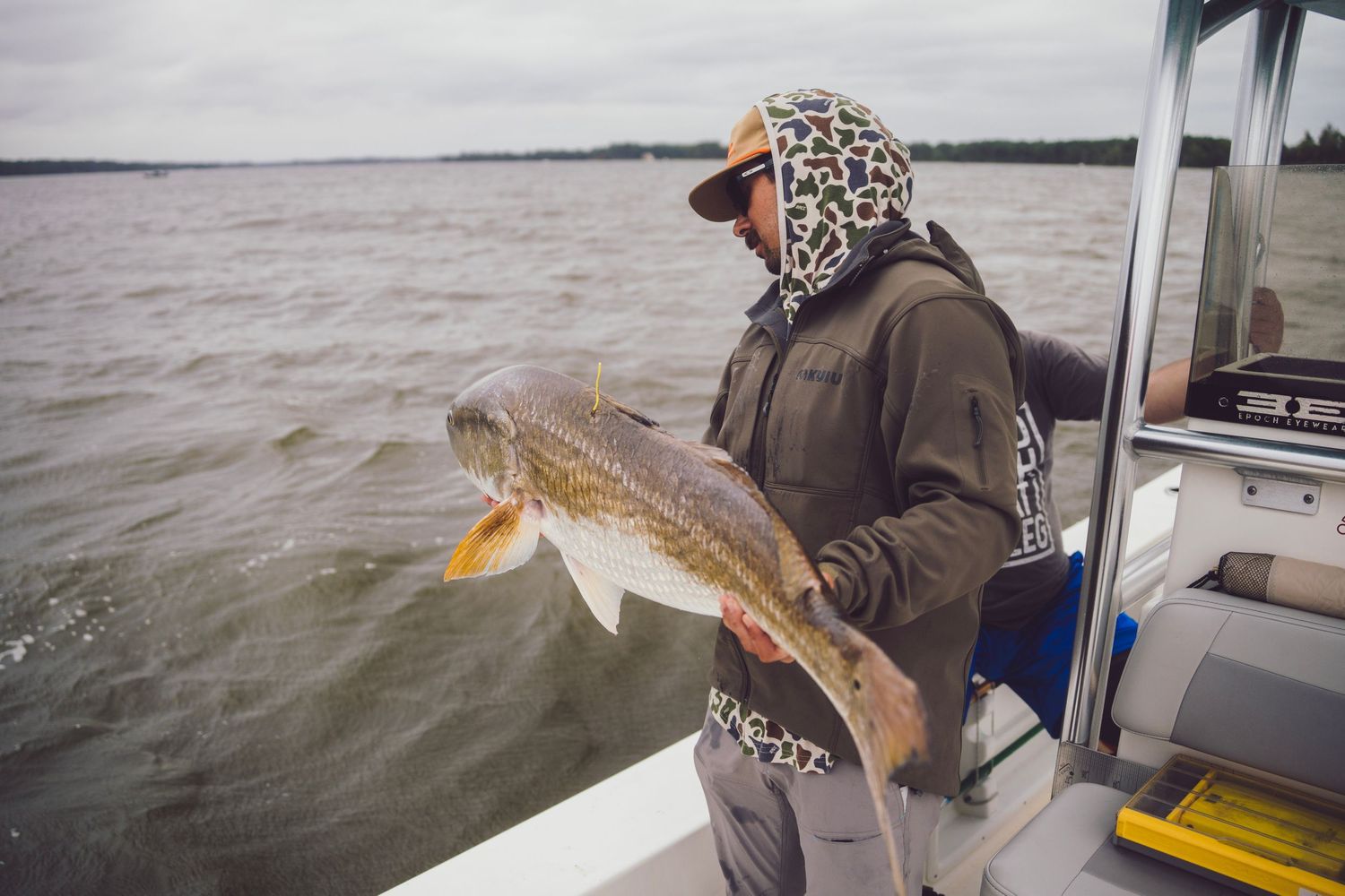 Angler holding a large redfish on a boat with choppy water in the background on a cloudy day.