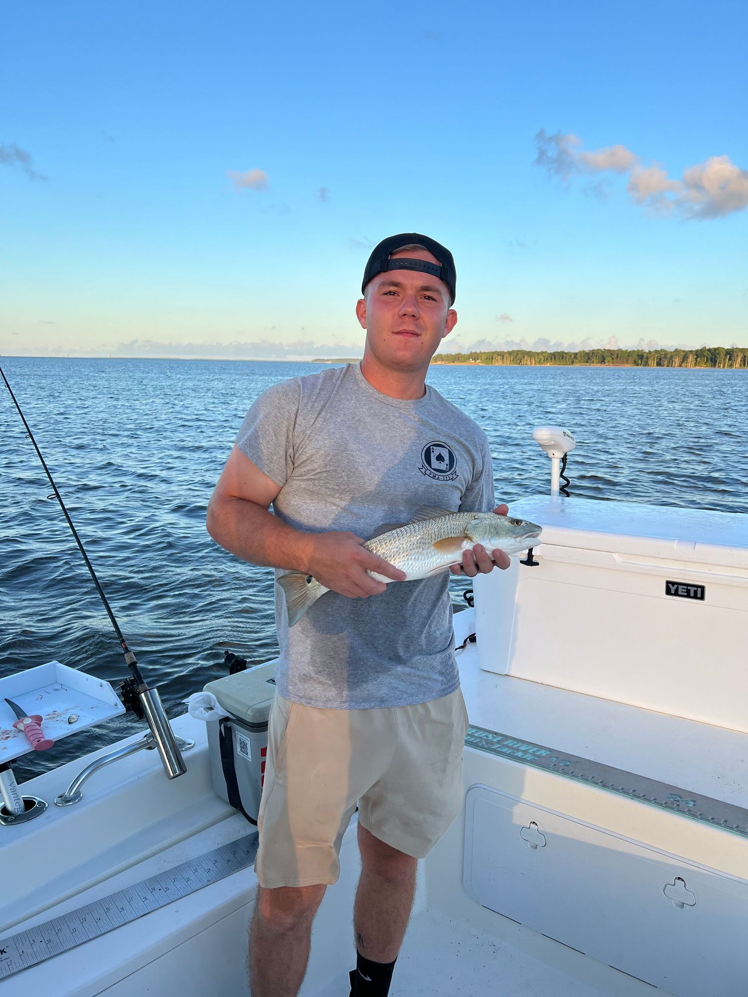 Angler in grey shirt holds small fish catch during evening boat outing.