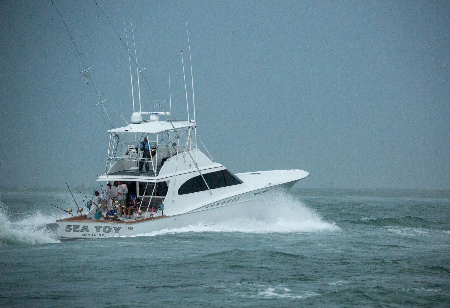 White sport fishing yacht charging through rough seas with spray flying from bow.