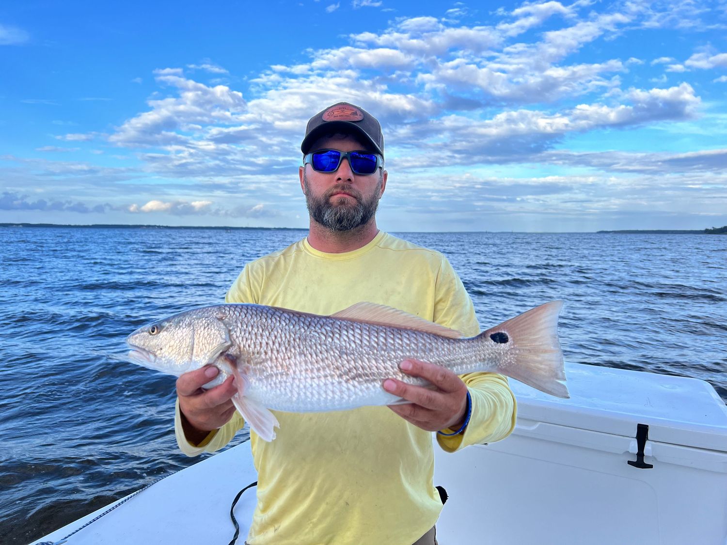 An angler on a boat proudly displays their freshly caught redfish against a backdrop of blue sky and ocean waters.