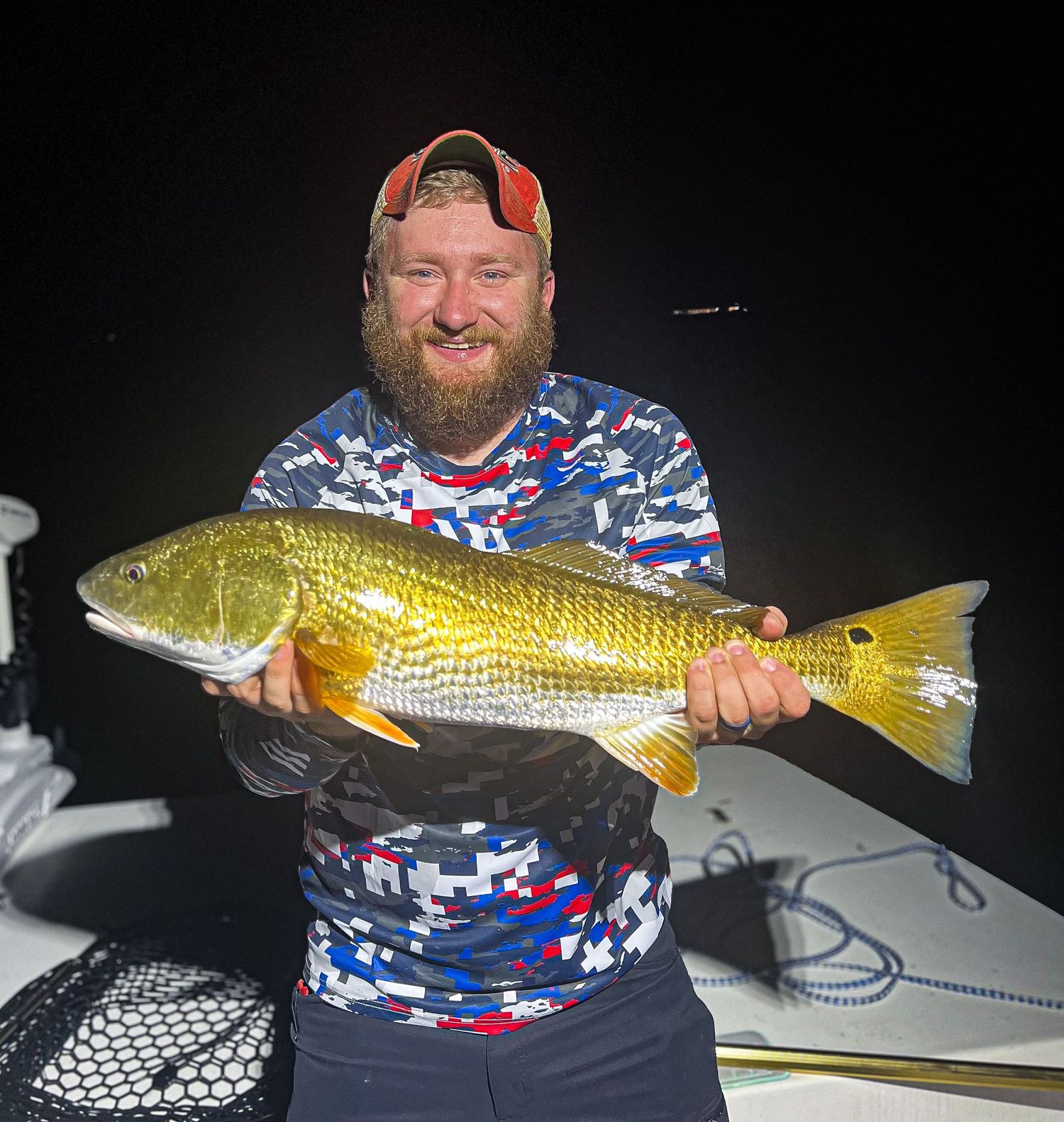 Angler in patriotic attire holding large golden redfish at night.