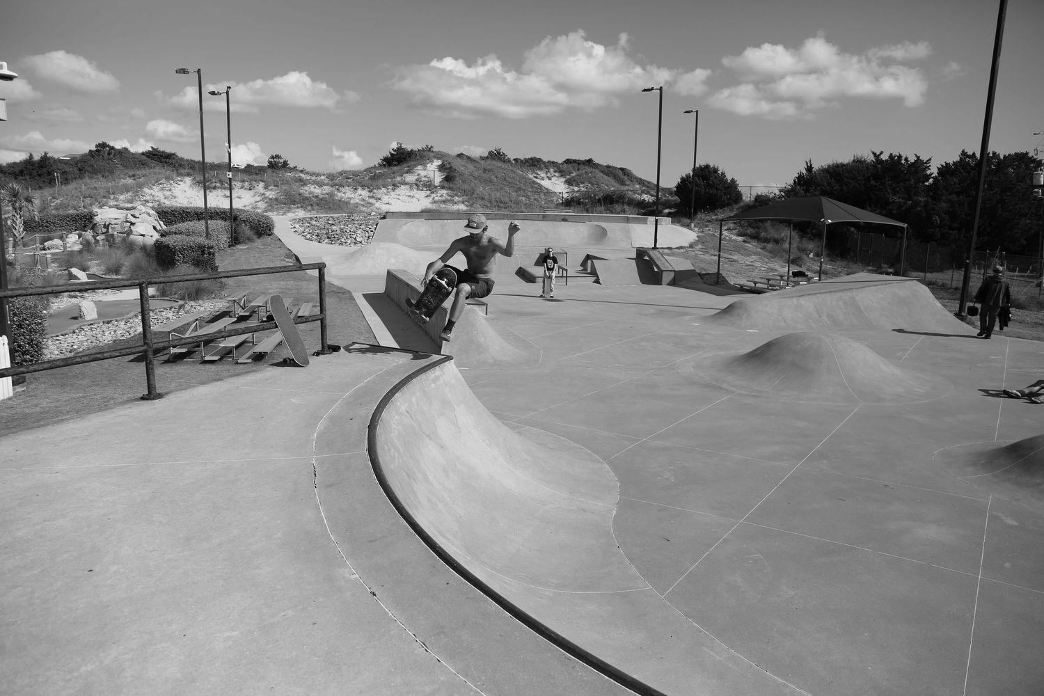 A skateboarder performs a trick on a curved concrete ramp at an outdoor skate park on a sunny day.