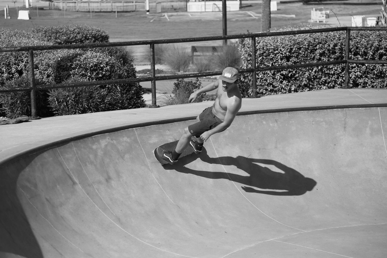 A skateboarder performs a trick in a concrete skate bowl casting a dramatic shadow in black and white photography.