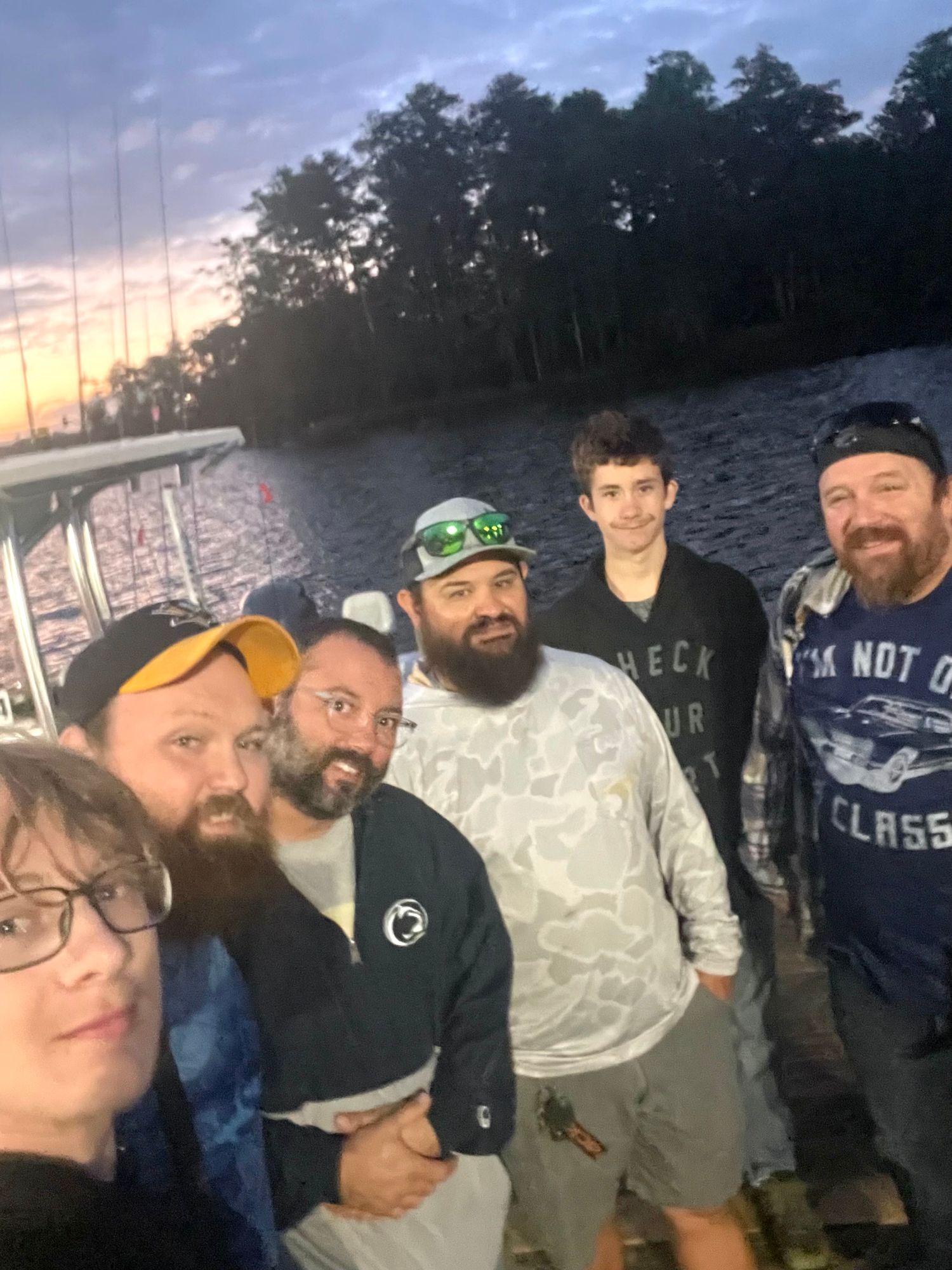Group of fishermen enjoying an end of trip photo outdoors with trees in the background.