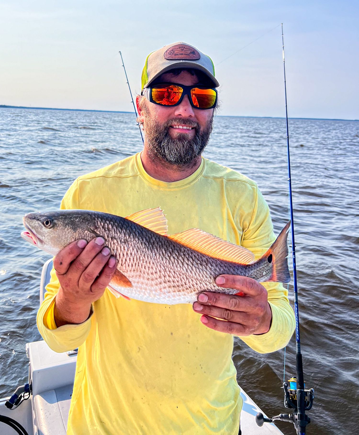 Angler in yellow shirt holding fresh-caught redfish on boat.
