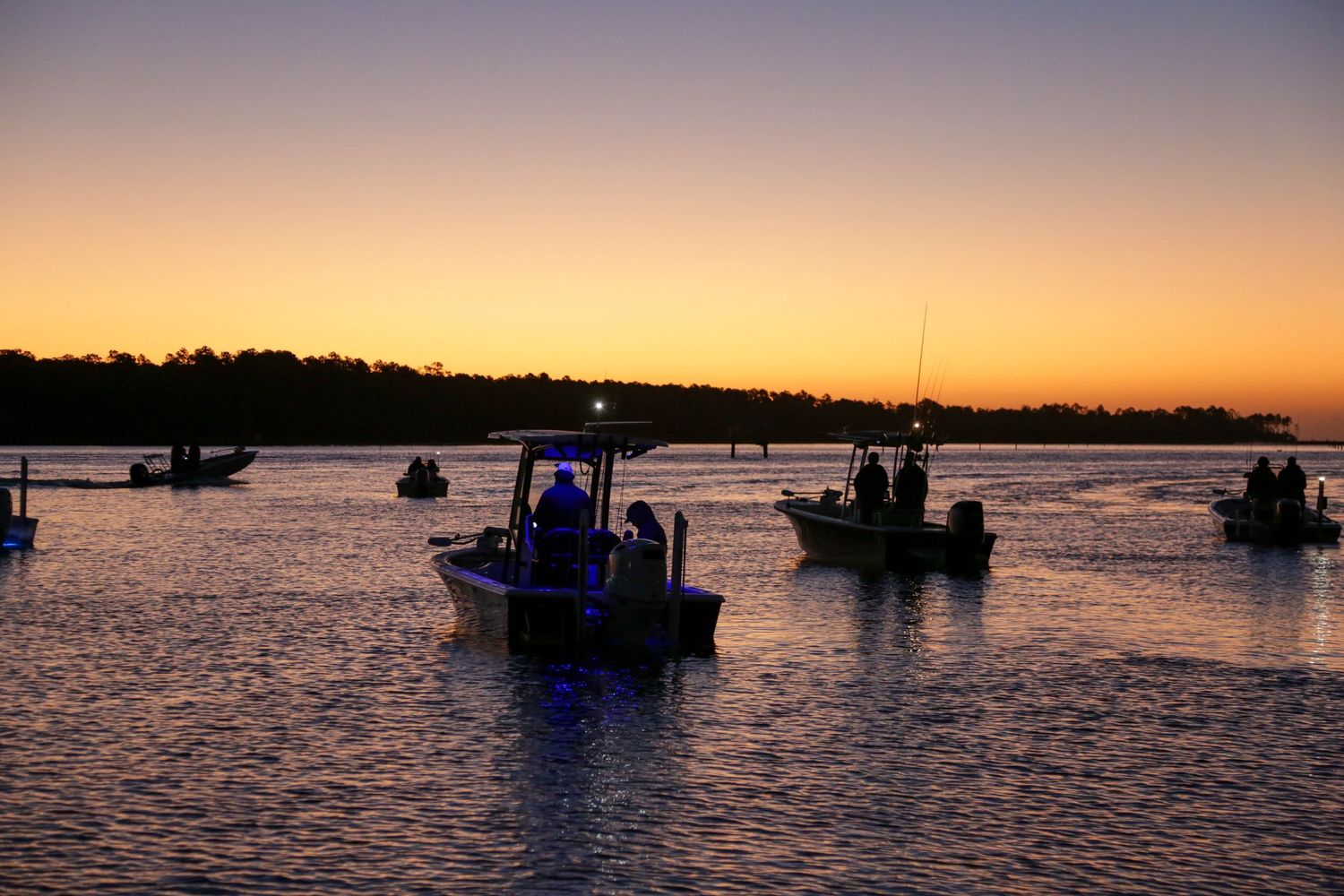 Fishing boats silhouetted against orange sky during sunset on calm waters.
