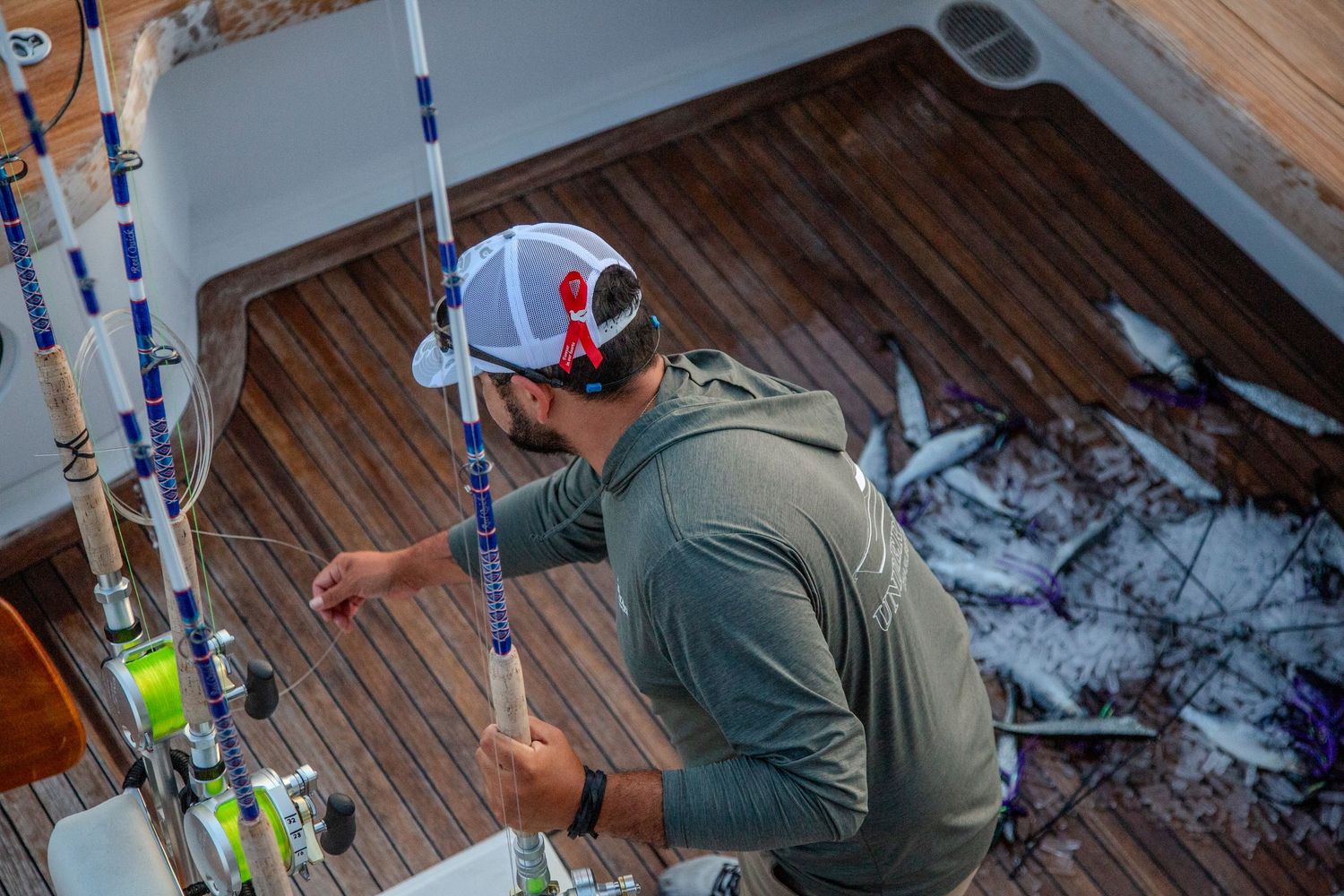 Man in cap sorting fishing rods on a boat deck with fresh-caught fish scattered nearby.