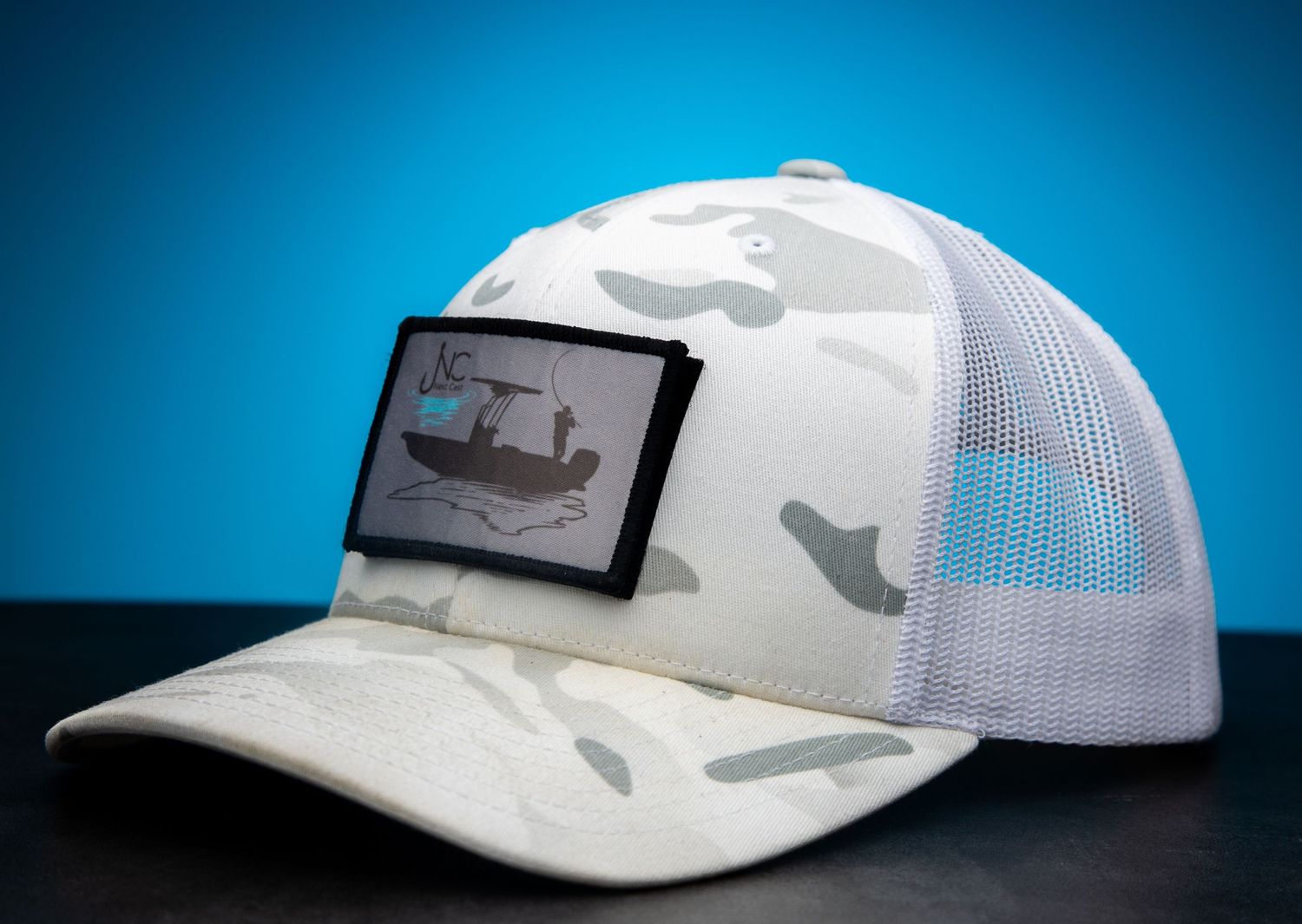 White camouflage trucker hat with mesh back panel against blue background.