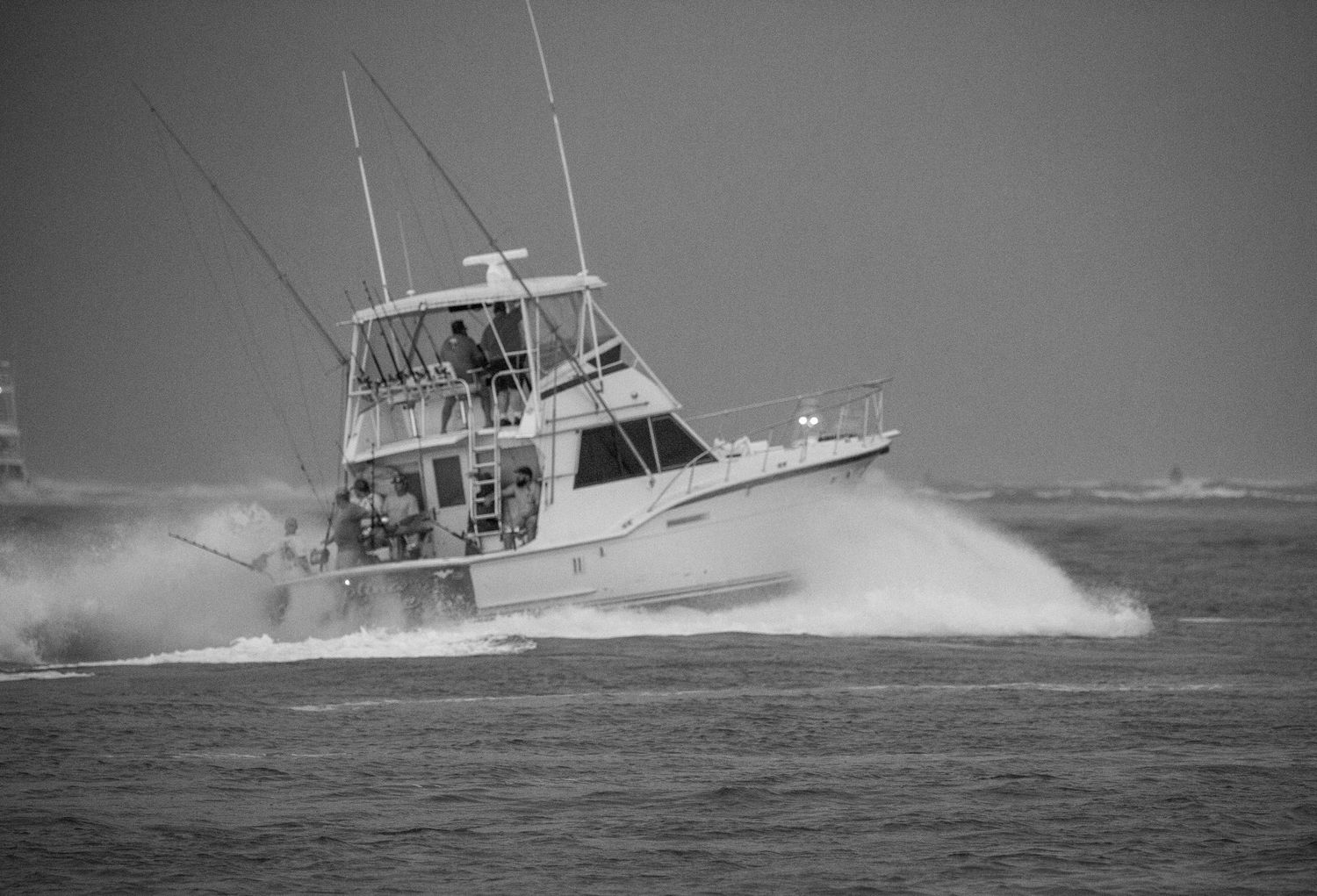 Black and white photo of a sport fishing boat crashing through waves during rough sea conditions.