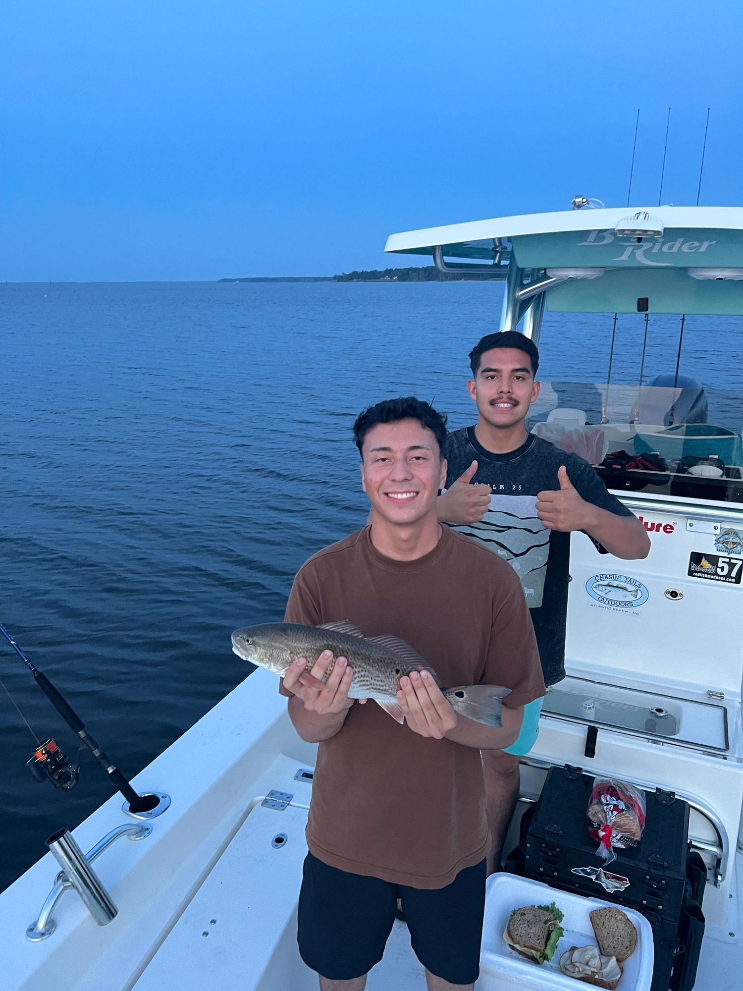 Two fishermen show off their catch on a sport fishing boat in clear blue waters.