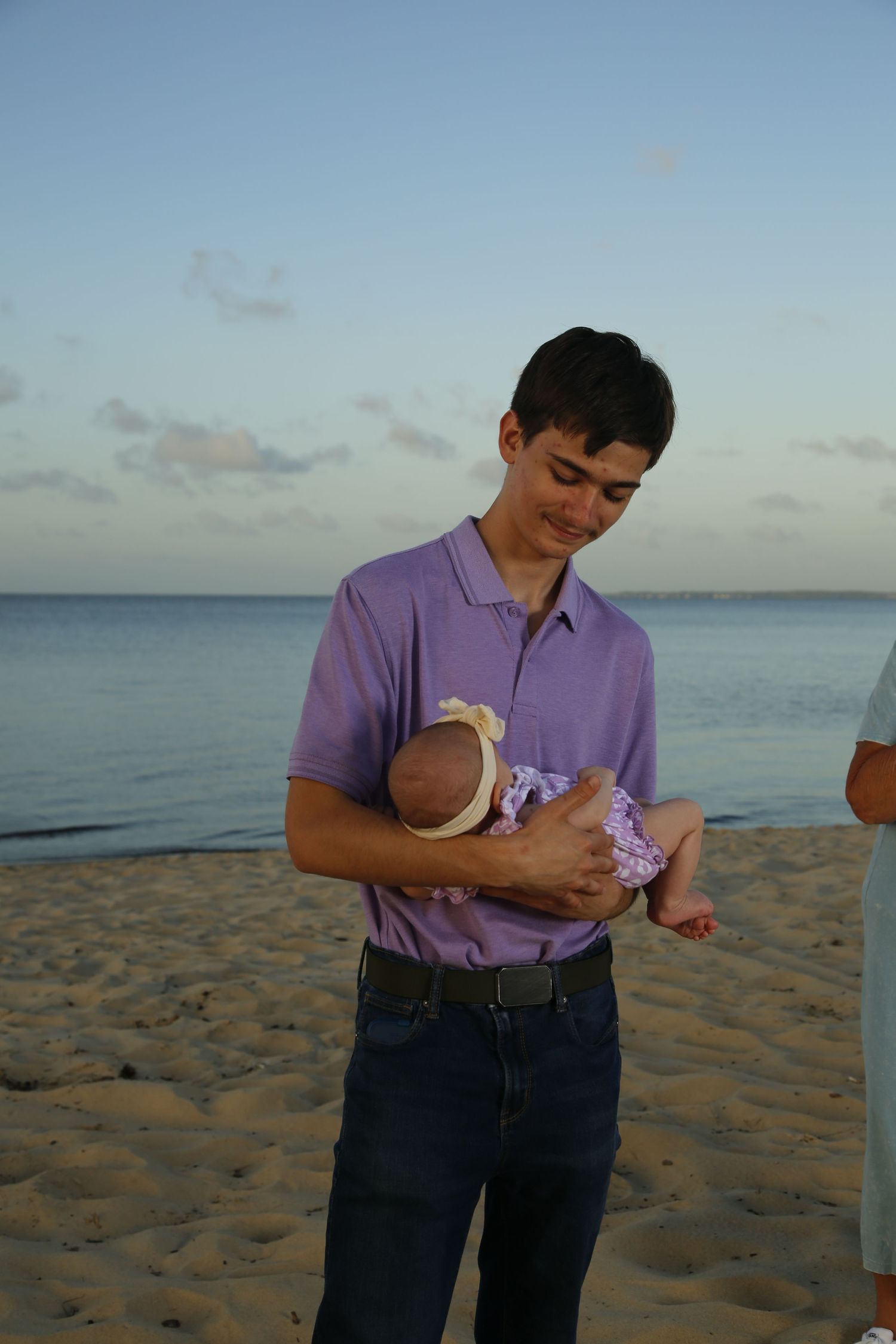 Person in purple shirt holding small baby on beach at sunset.