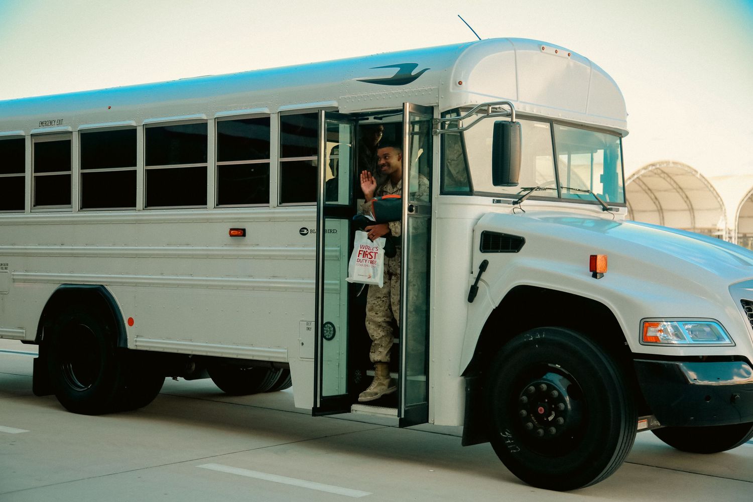 A series of white school buses parked in a row at a transportation facility.