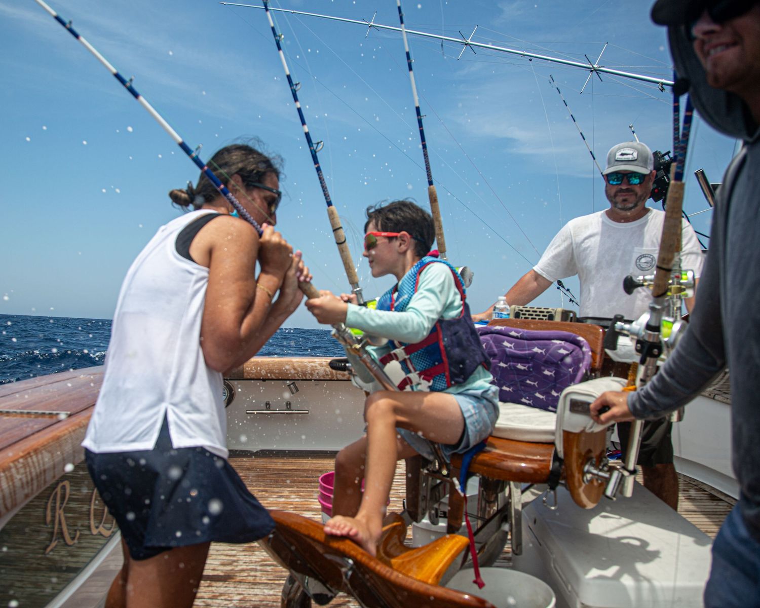 Group of people enjoying deep sea fishing on a boat, with fishing rods and ocean views on a sunny day.