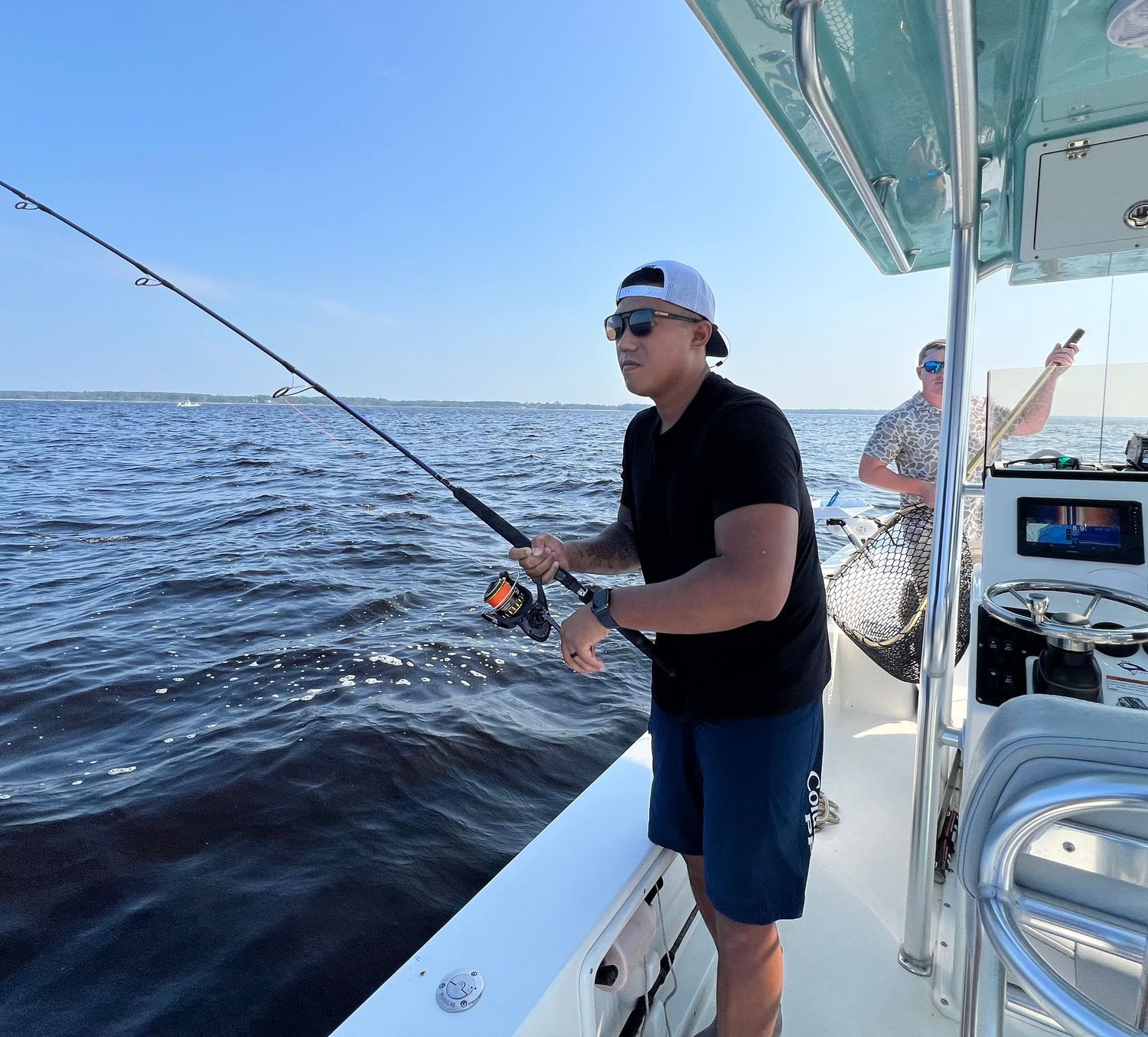 Anglers reeling in catches from a white fishing boat deck on a sunny day at sea.