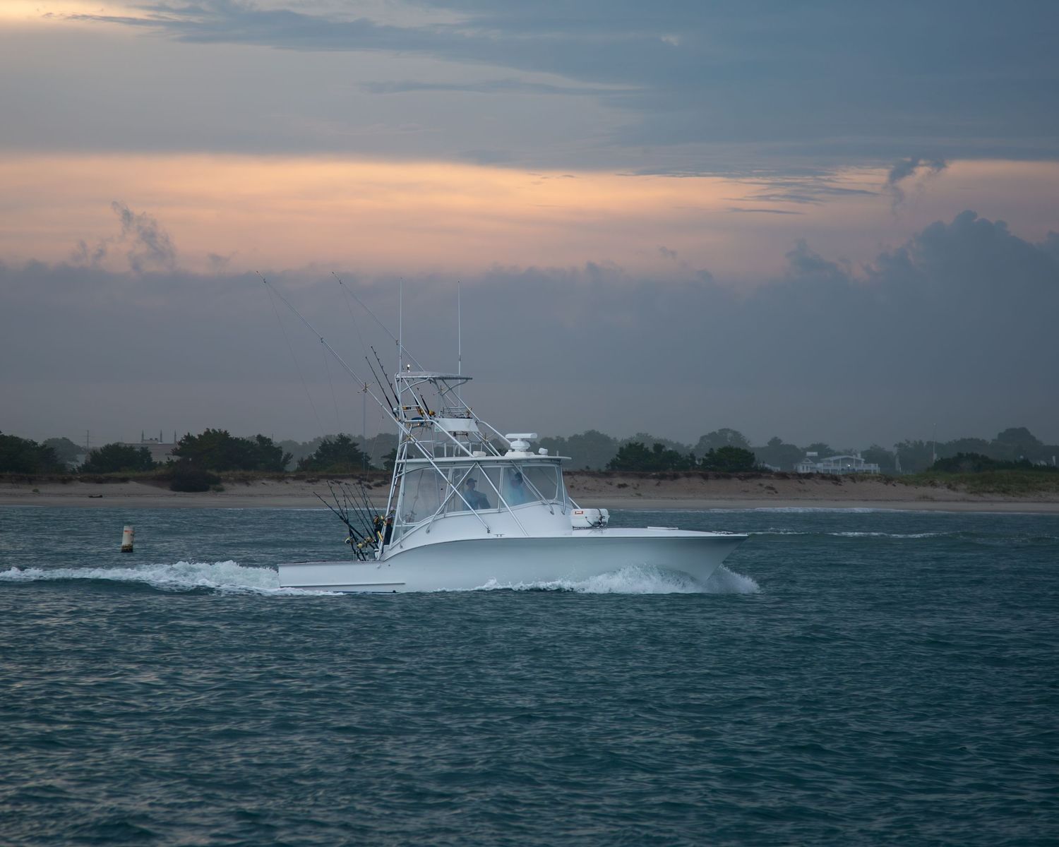 Sport fishing boat cruising through coastal waters at sunset with dramatic orange sky.