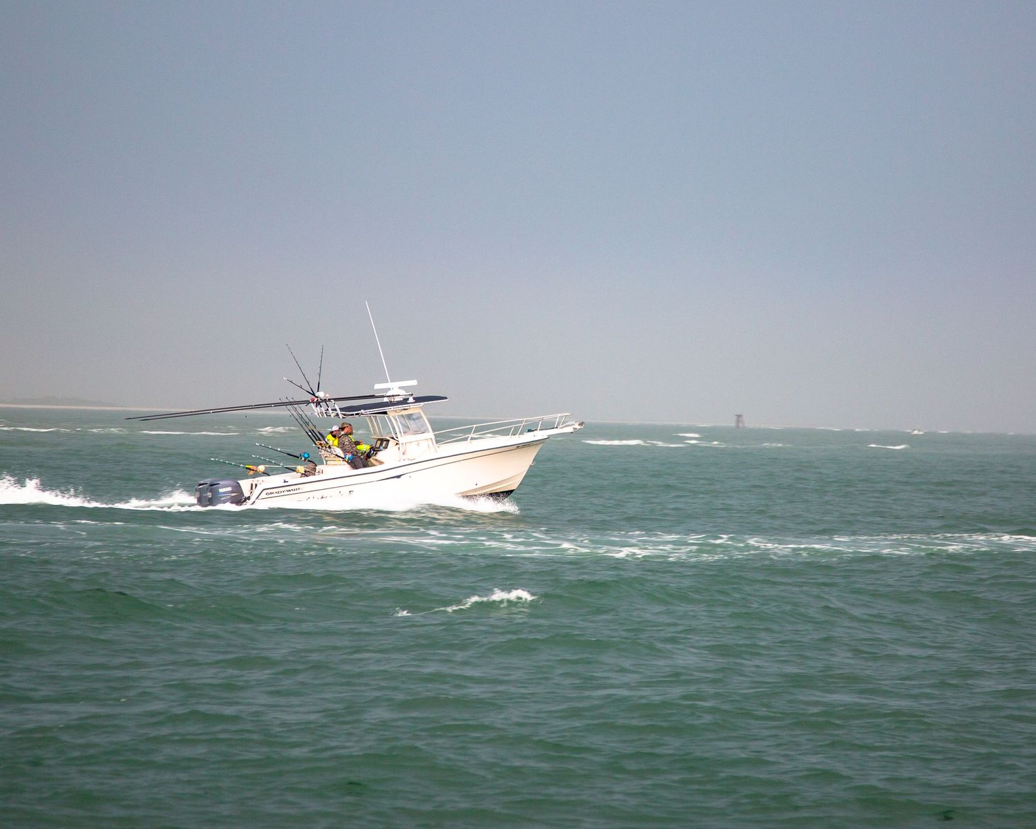 Sport fishing boat navigates through rough green waters near the shoreline.