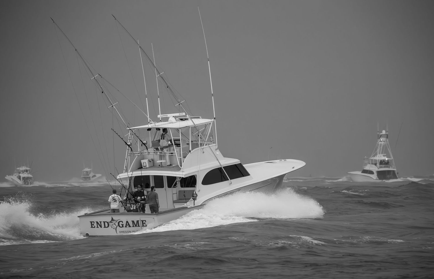 Black and white image of sportfishing boat racing past lighthouse in rough seas.