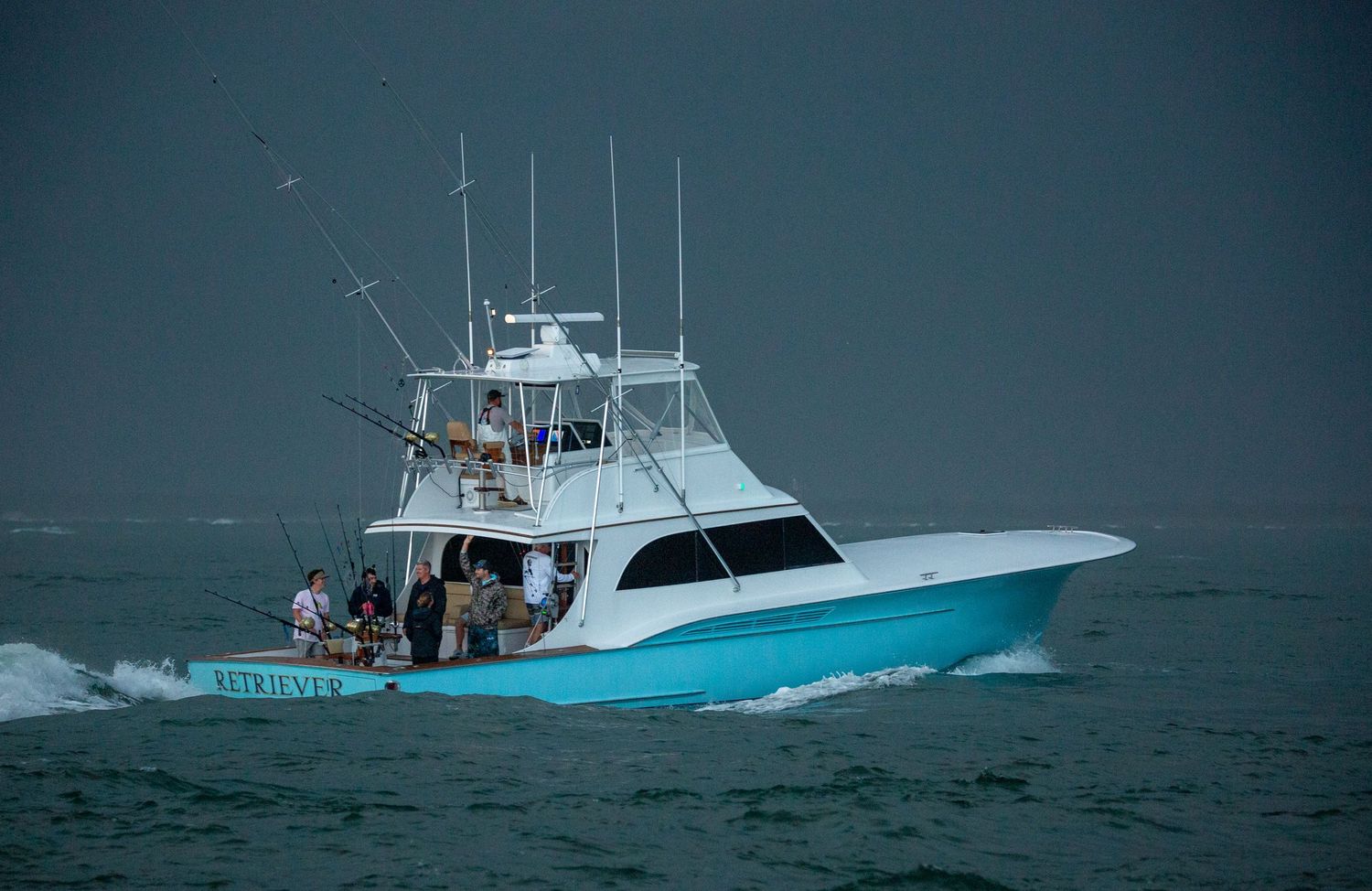 Blue and white sport fishing yacht navigating through rough ocean waters on a cloudy day.