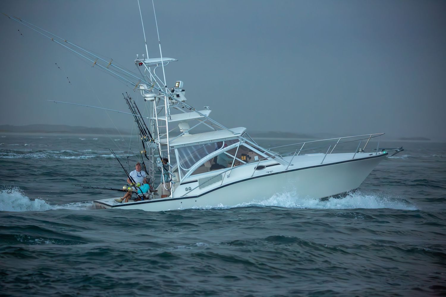 Fishing boat cutting through rough seas with large wake behind it.