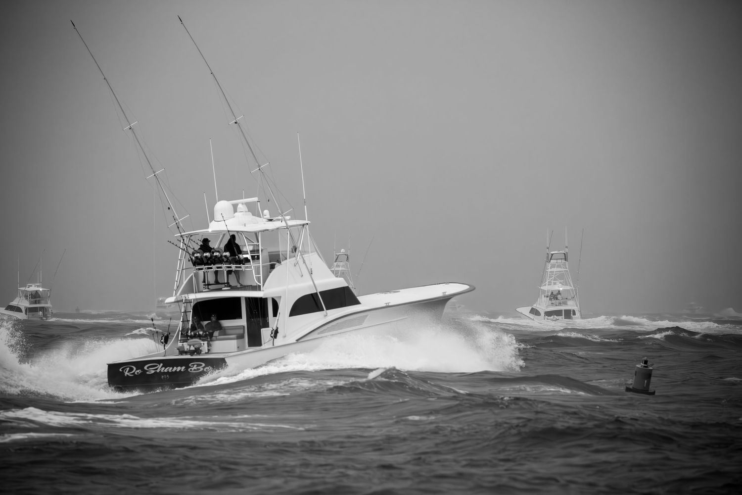 Black and white photo of sport fishing boat cutting through large waves at sea.