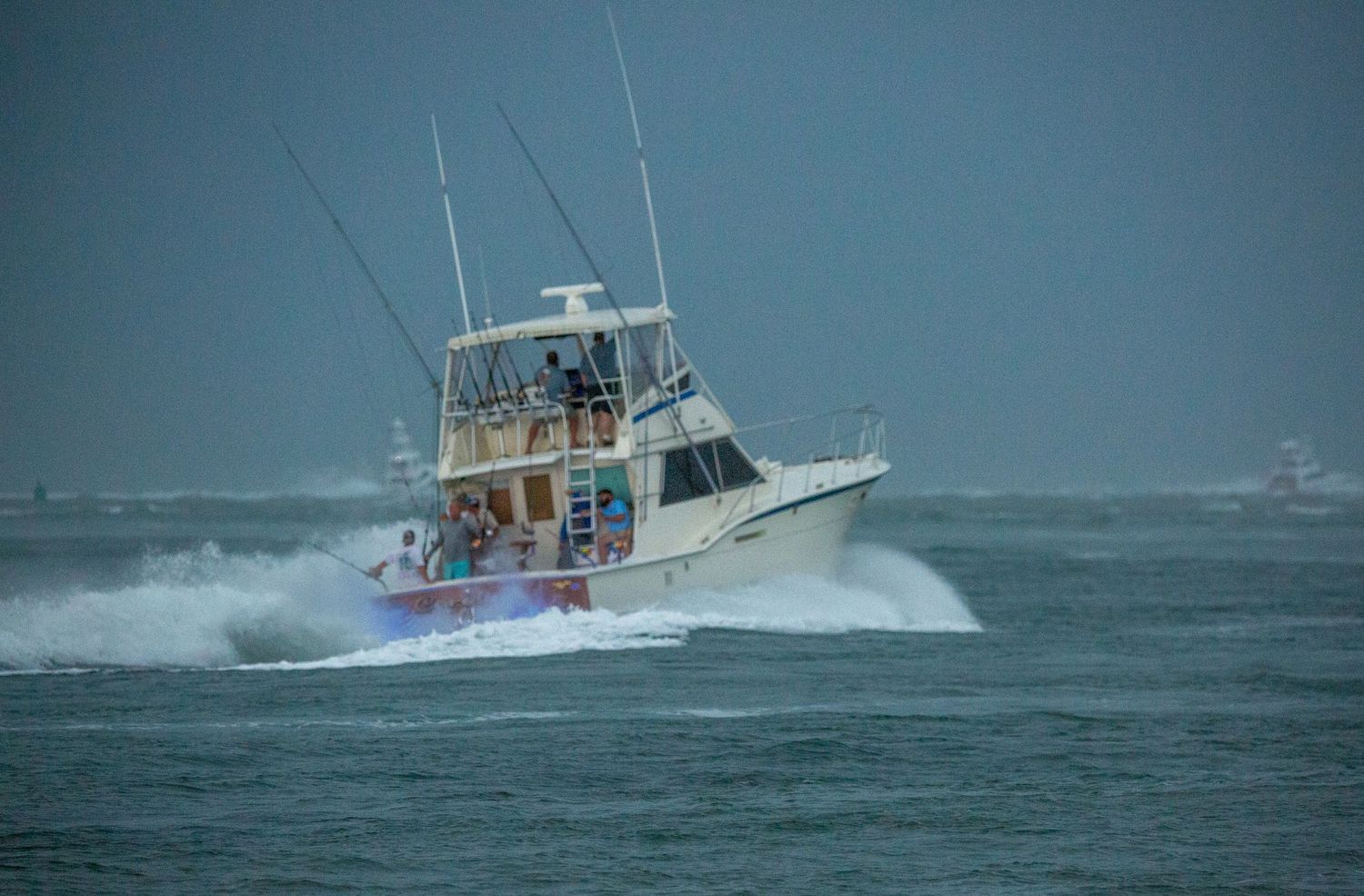 Sport fishing yacht creates large spray while navigating through stormy ocean waters.