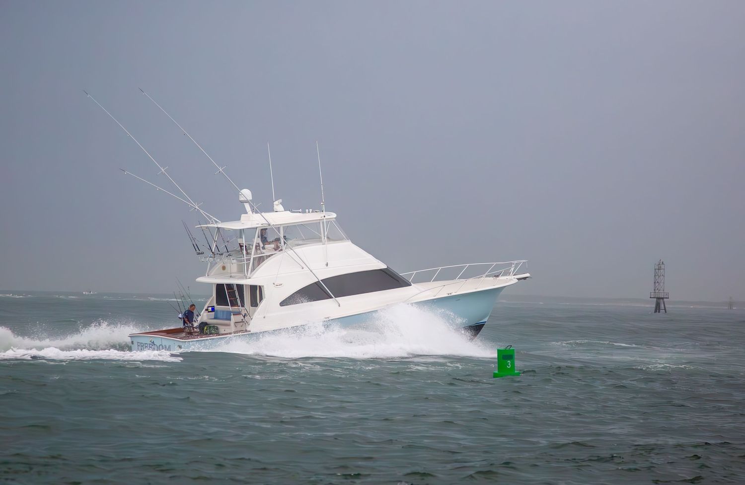 Luxury sportfishing yacht plowing through turbulent ocean waters near navigation markers.