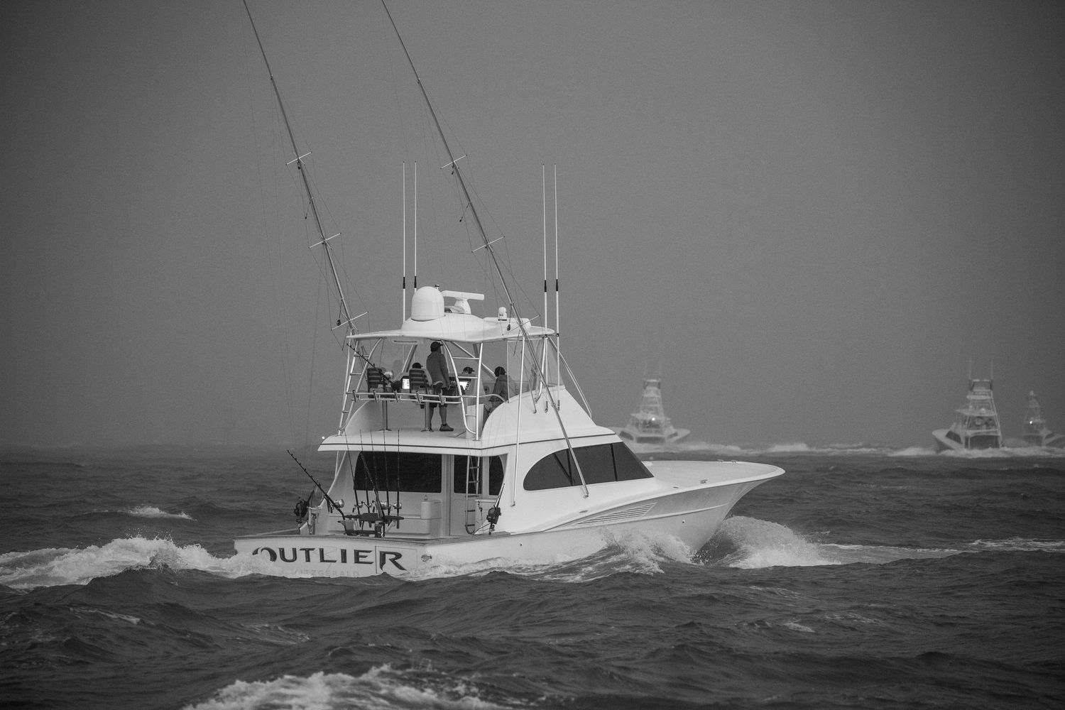 Luxury fishing boats powering through turbulent ocean waves in gray weather.