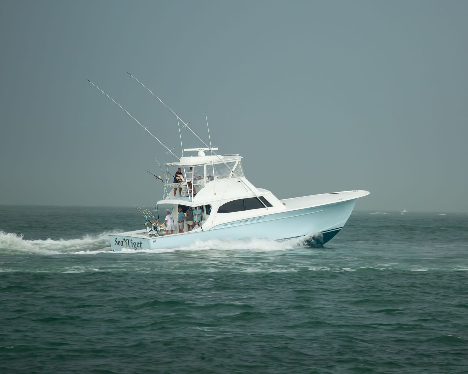 White sport fishing yacht speeding through turquoise waters with fishing equipment ready.