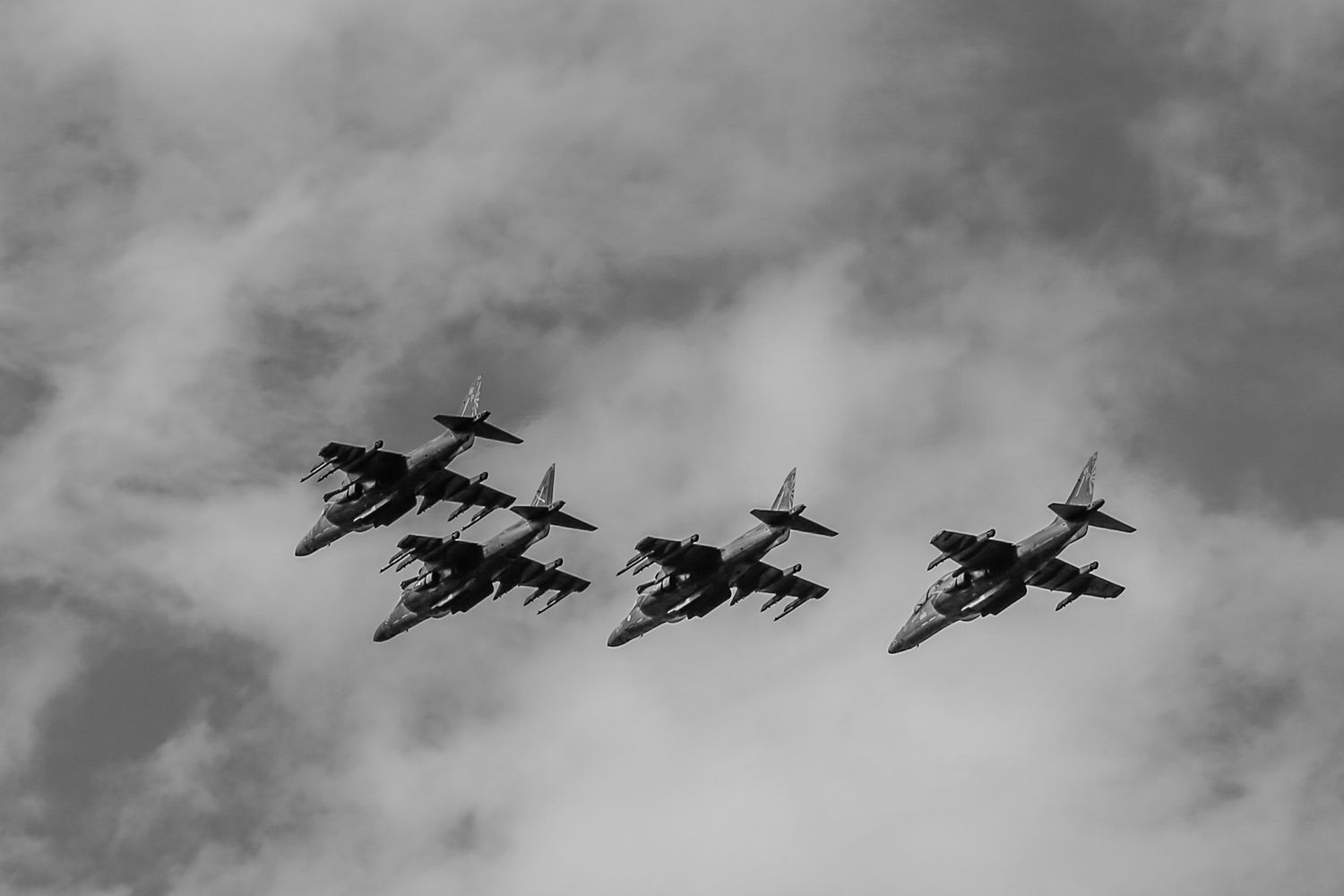 Four military jets flying in tight formation through cloudy skies in black and white photography.