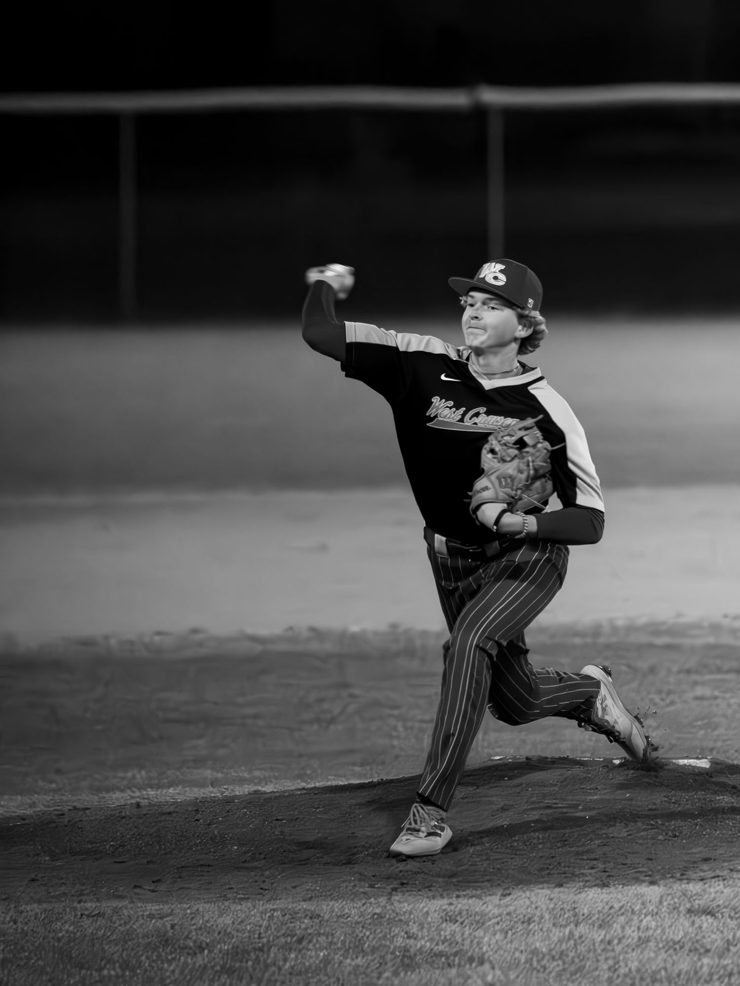 Baseball player executing dramatic pitching motion during a game in black and white photography.