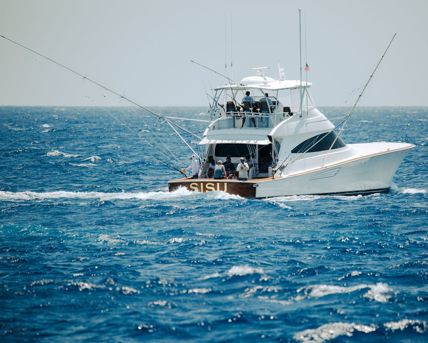 White sport fishing boat named SISU cruising on deep blue ocean waters with fishing rods extended.