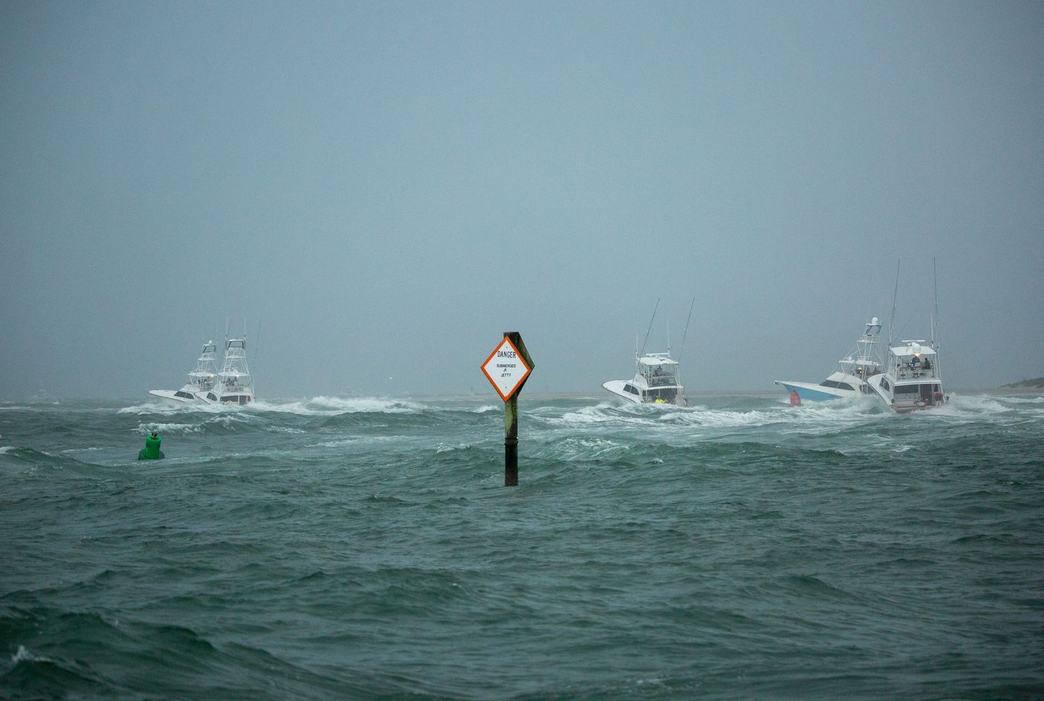 Sport fishing vessels navigate around channel markers in choppy seas during overcast weather.