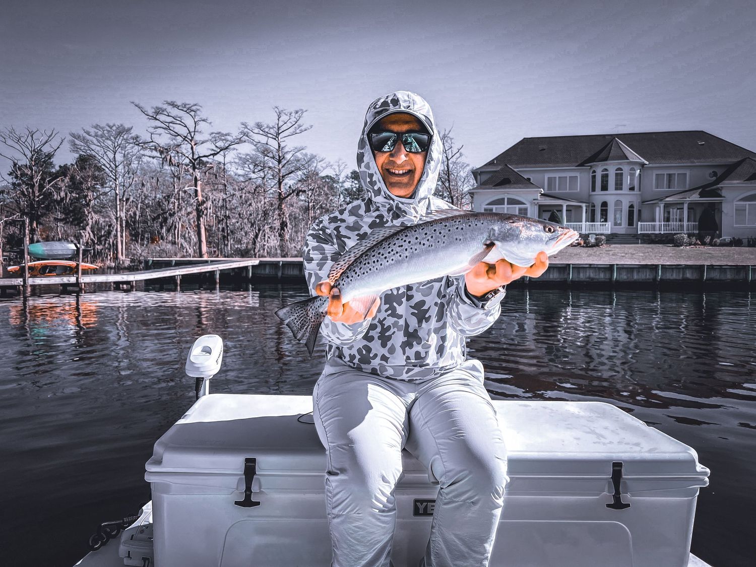 Angler shows off red drum catch in front of waterfront home in black and white effect.