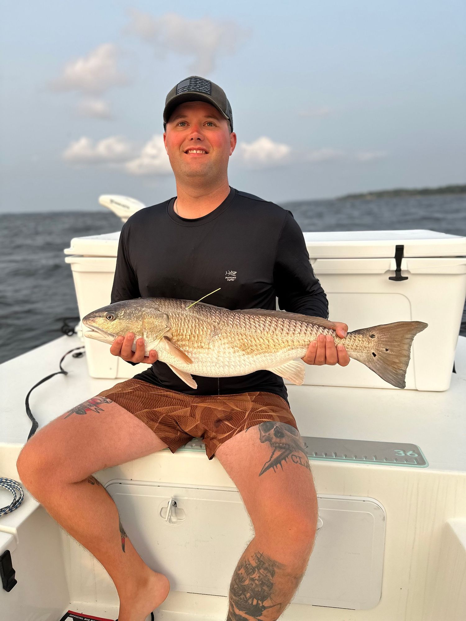 Man on boat holding large redfish caught while saltwater fishing on open water.