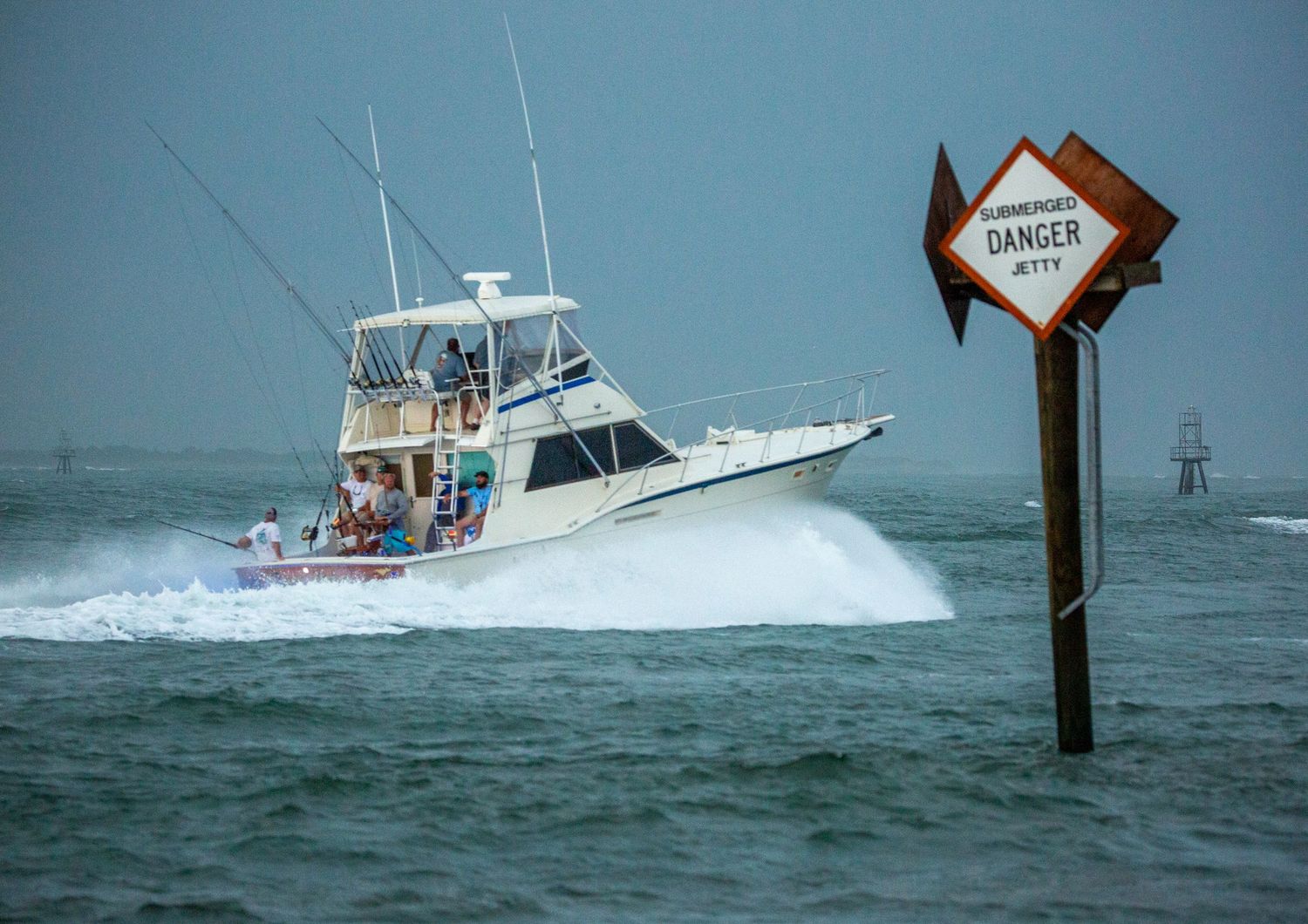 A fishing boat speeds past a diamond-shaped danger sign marker in choppy waters.