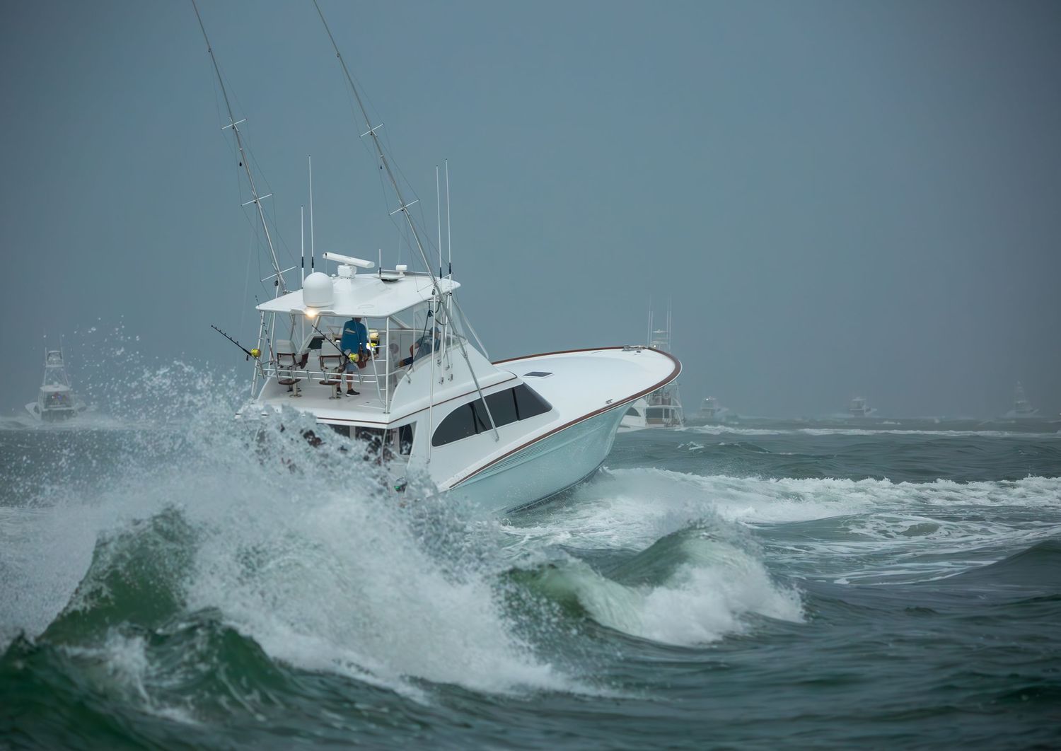 White sport fishing boat crashes through large ocean waves in rough conditions.