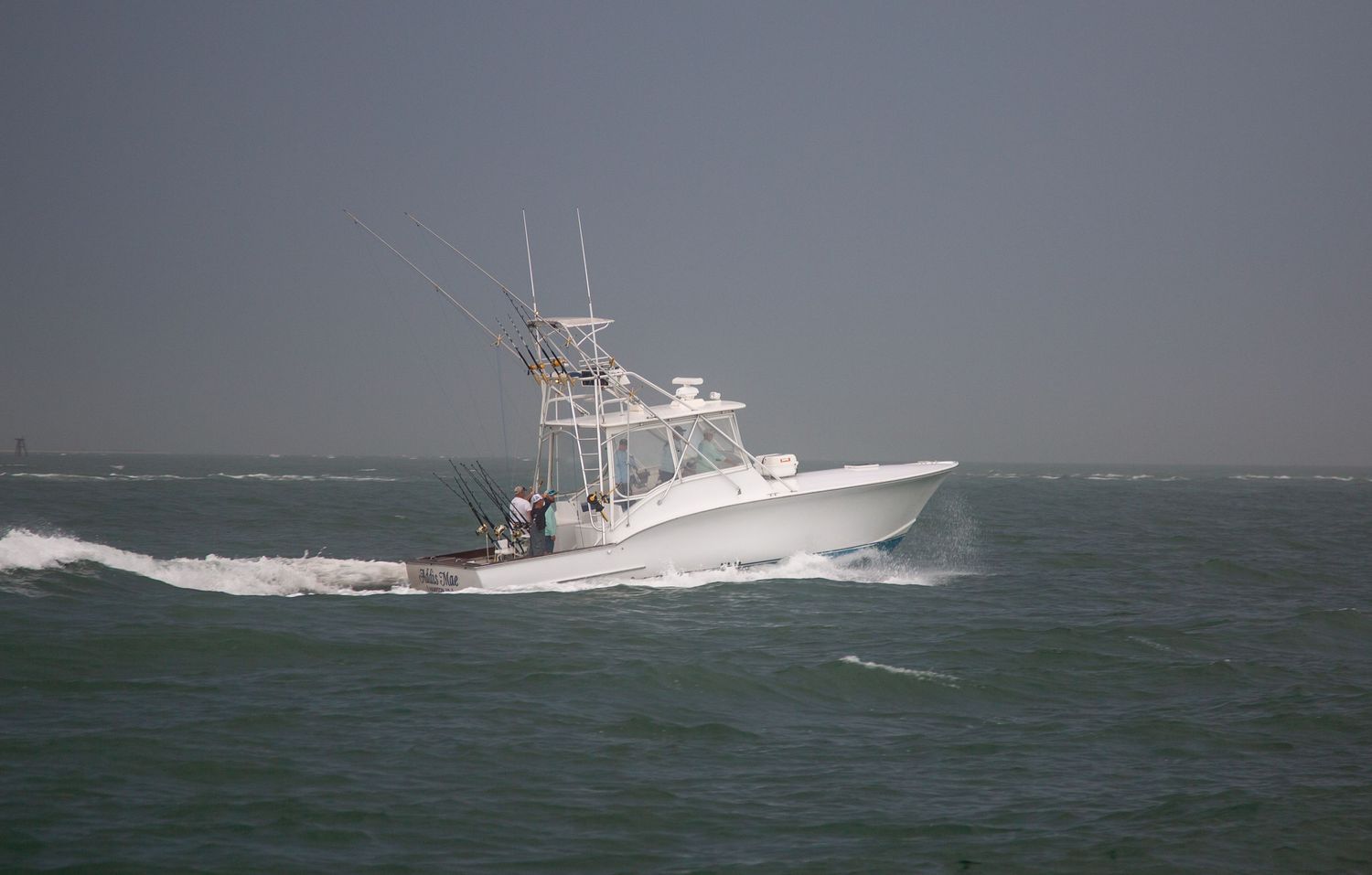 White fishing boat powering through choppy ocean waters on an overcast day.