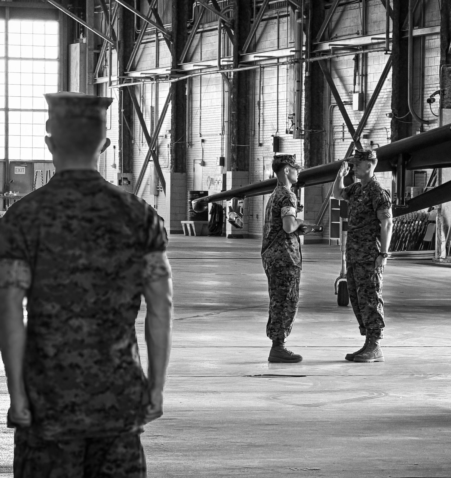Black and white photo of U.S. Marines in camouflage uniforms standing at attention inside a military hangar.