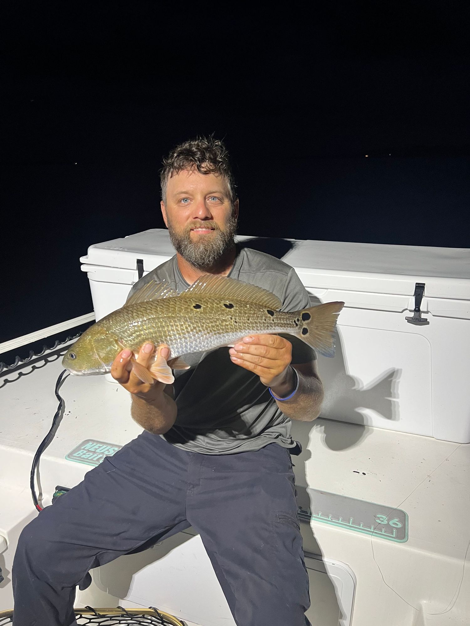 Angler showing prized catch of carp fish while fishing from boat during nighttime expedition.