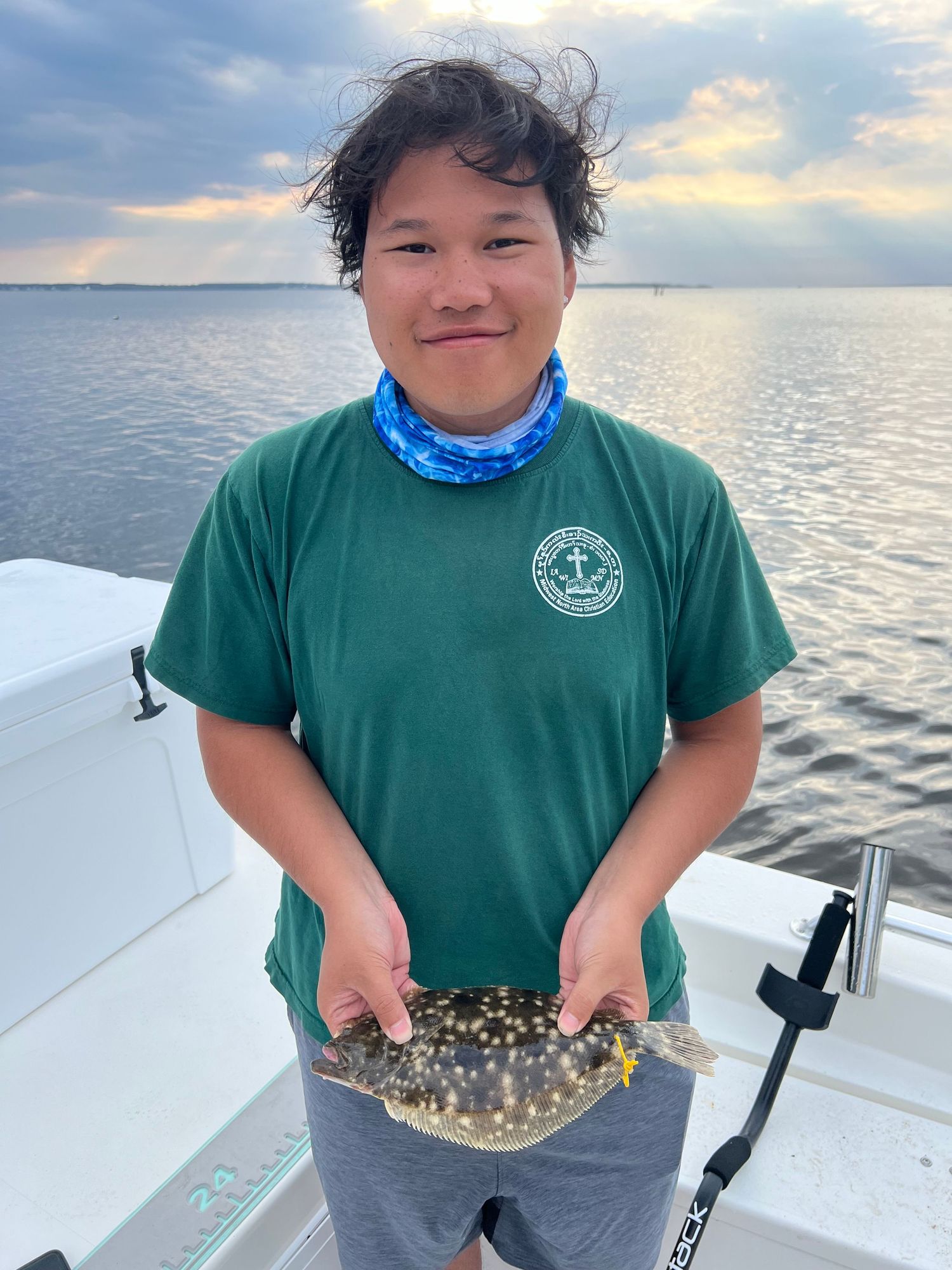 Angler on boat showing off a spotted flounder catch during golden hour.