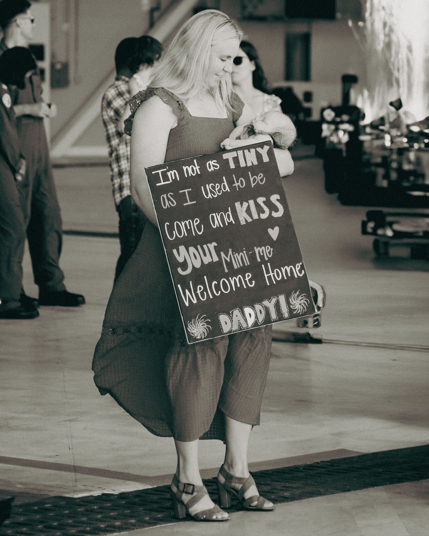 A series of black and white images showing someone holding welcome home signs at what appears to be an airport terminal.