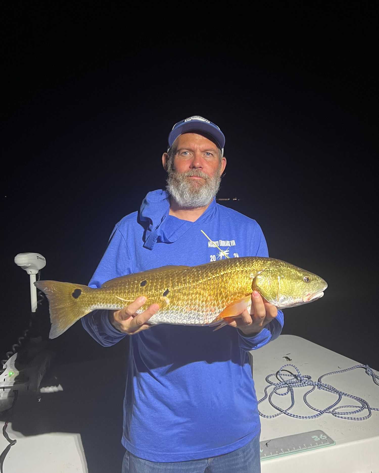 Nighttime angler displays golden redfish catch on boat deck.