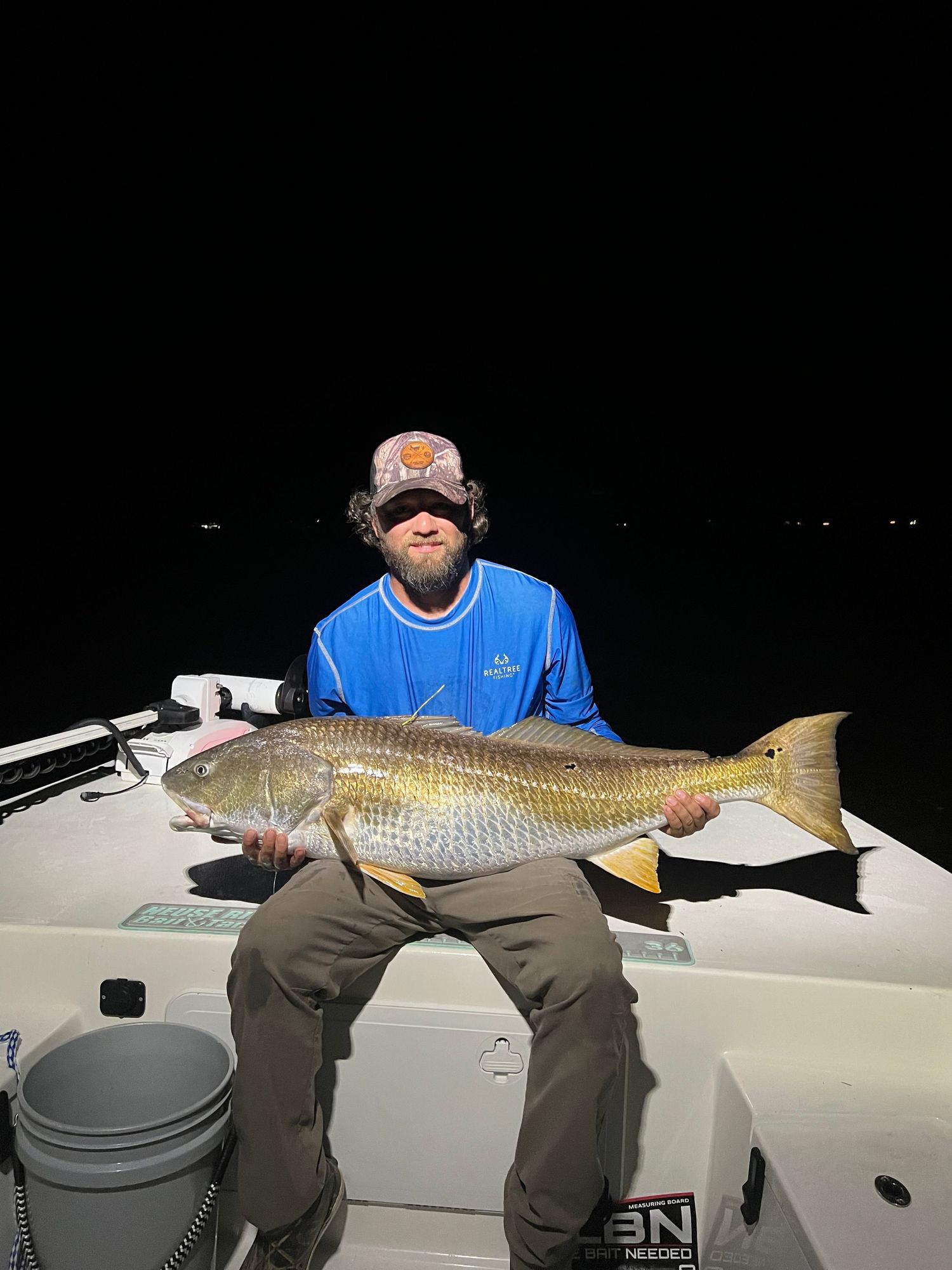 Impressive red drum fish held up for display against dark nighttime waters.